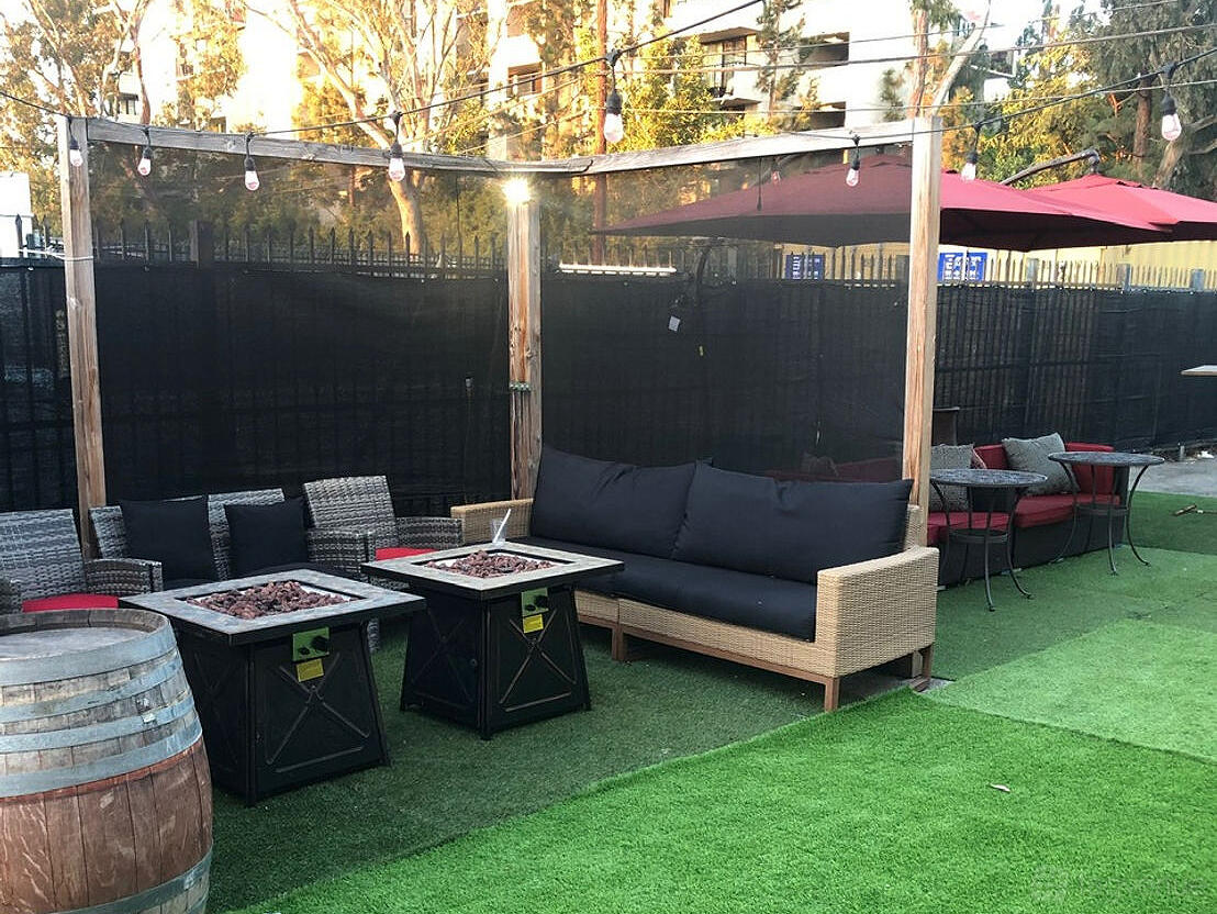 An outdoor gallery patio with string lights, wicker seating, fire tables, and artificial grass at The Creative House.