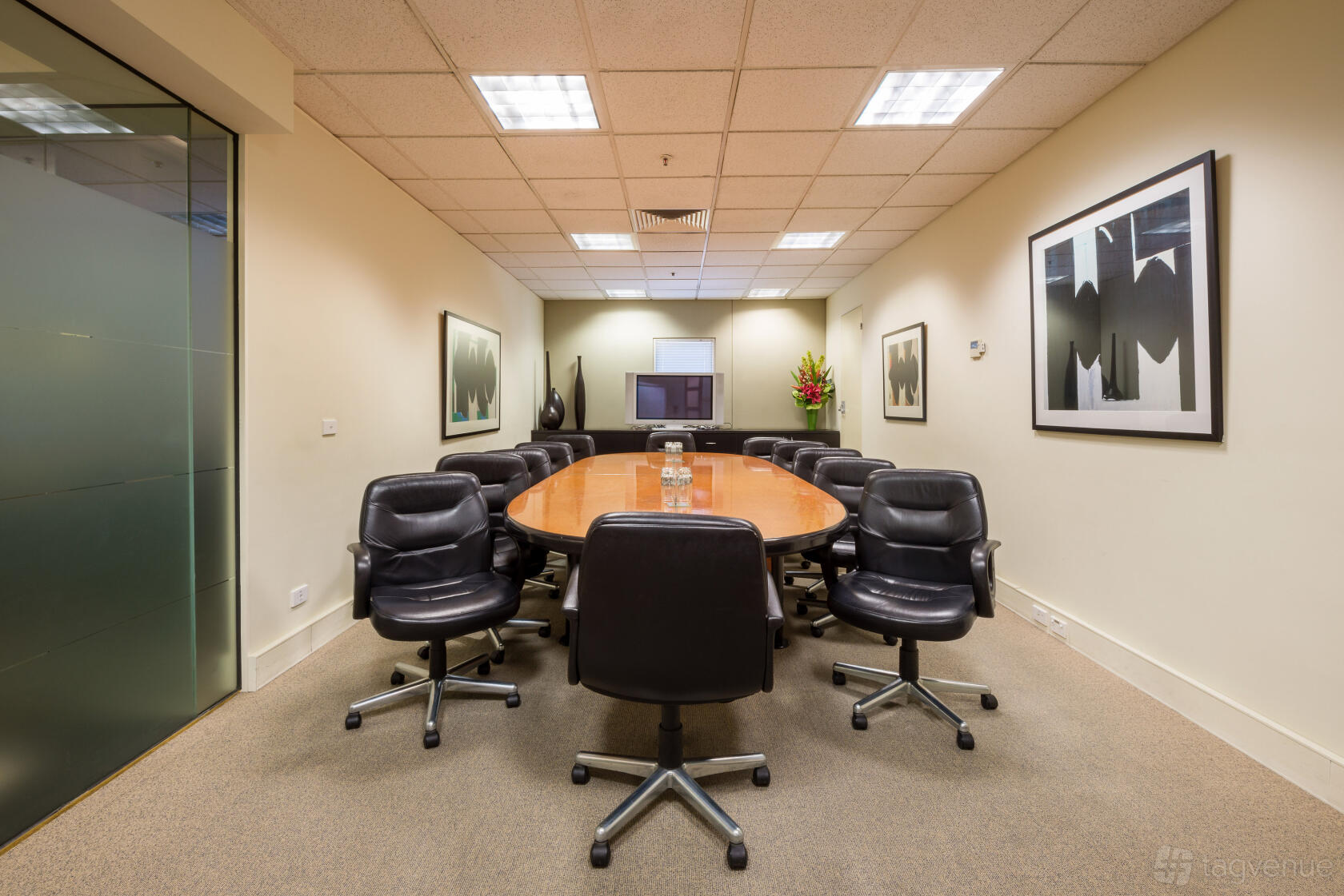A conference centre meeting room with an oval wooden table, black leather chairs, and wall art at @workspaces Toorak.