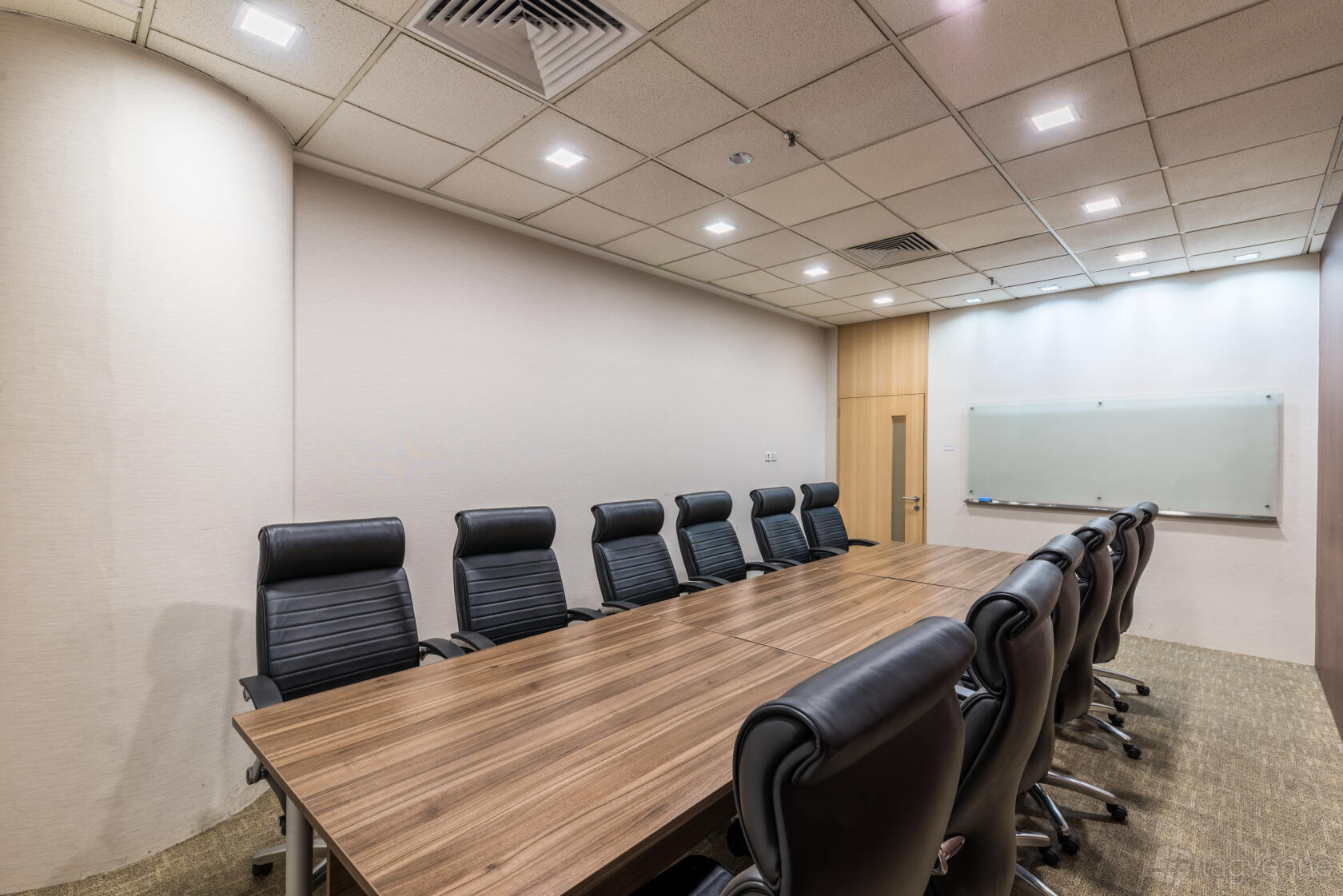A meeting room with a long wooden table, black leather chairs, and a whiteboard at The Company Singapore.