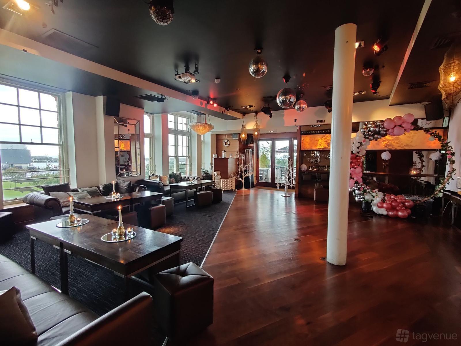 A bar in a restaurant with floor-to-ceiling windows, dark leather seating, hardwood floors, and disco balls at Wrights Findlater Howth.