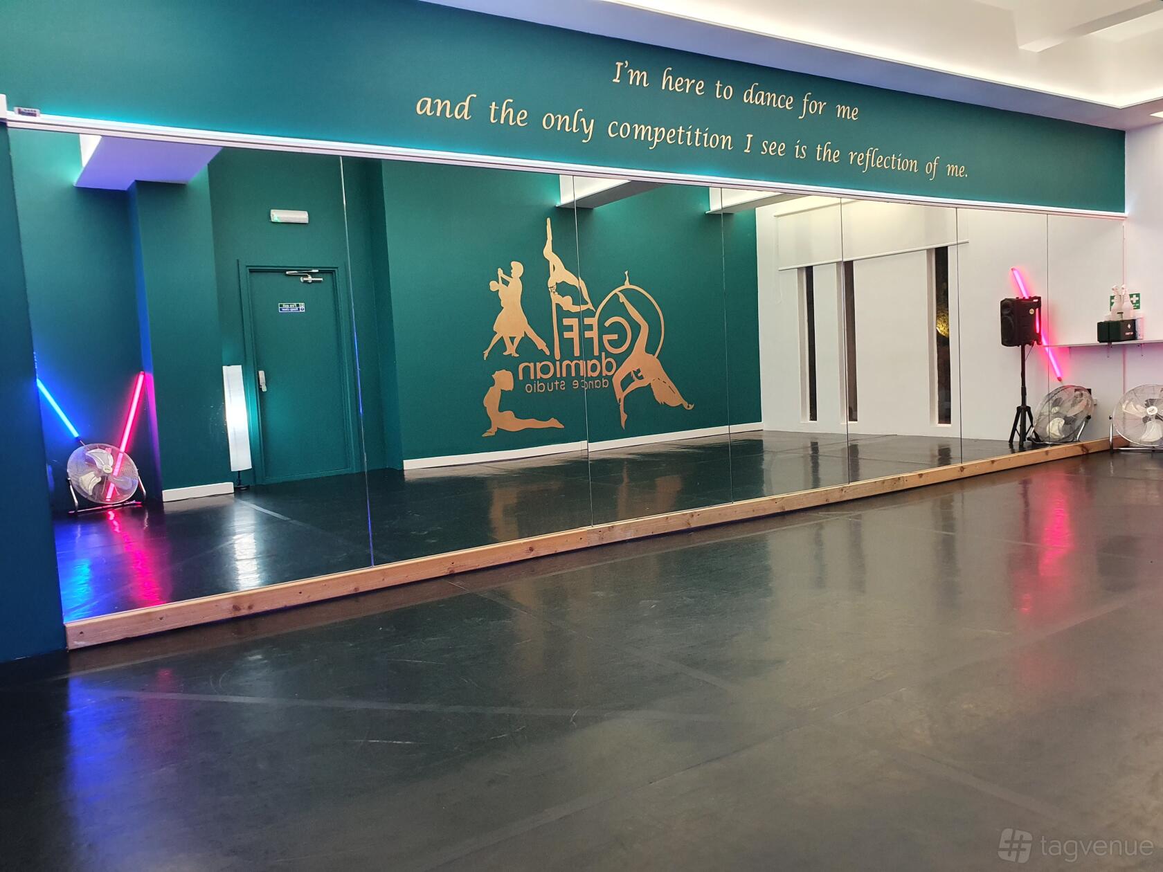 A rehearsal room with a full mirrored wall, ballet barre, teal accent wall, and motivational text at GFFdamian Dance Studio.