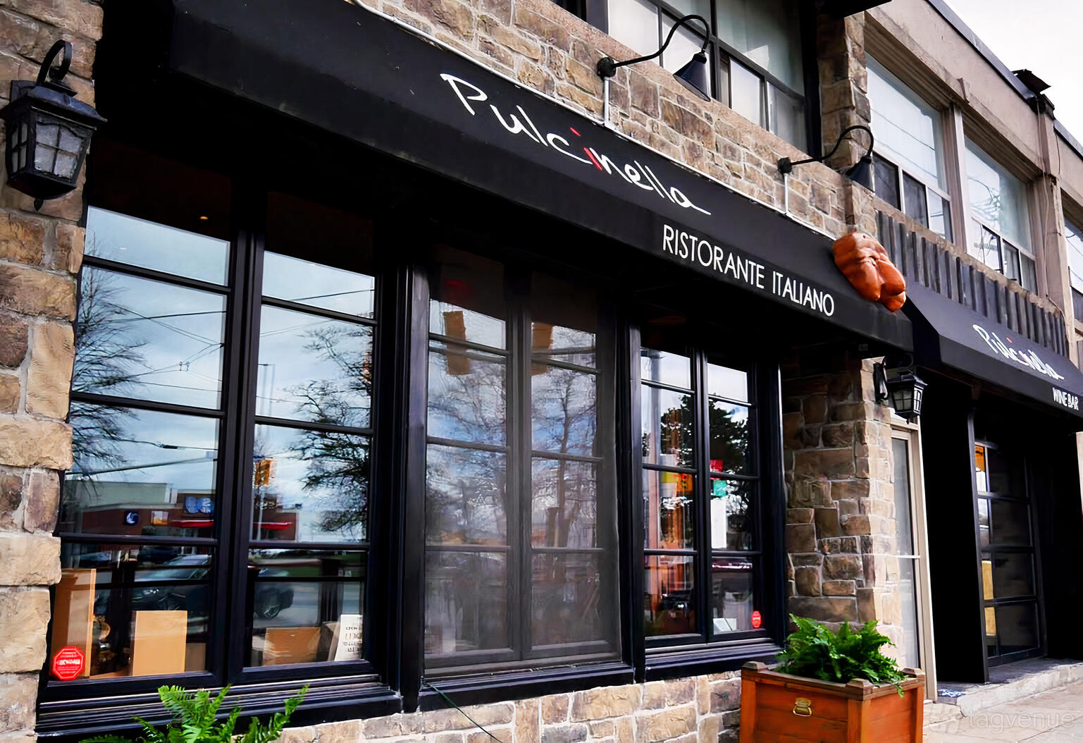 A restaurant exterior with stone walls, large black-framed windows, and a black awning at Pulcinella.