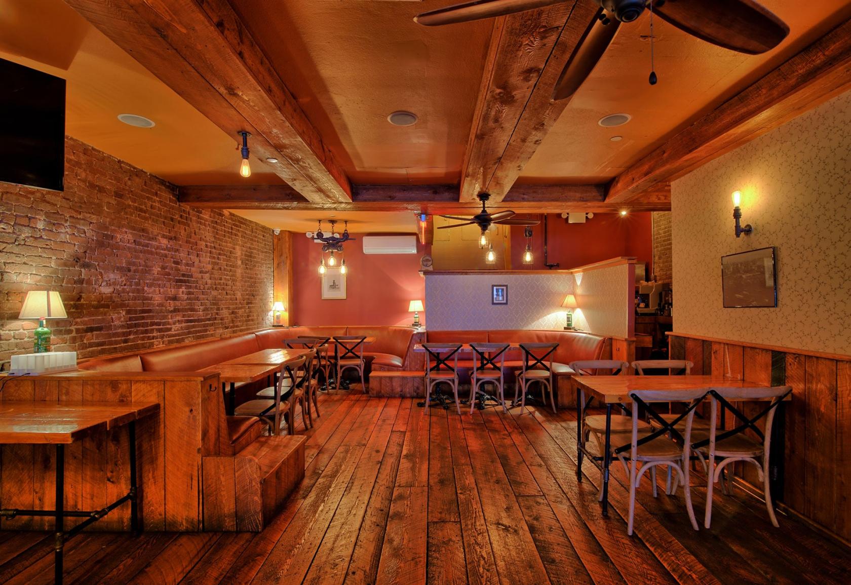 A lounge with exposed brick walls, wooden beams, and leather banquettes at Monk McGinn's.