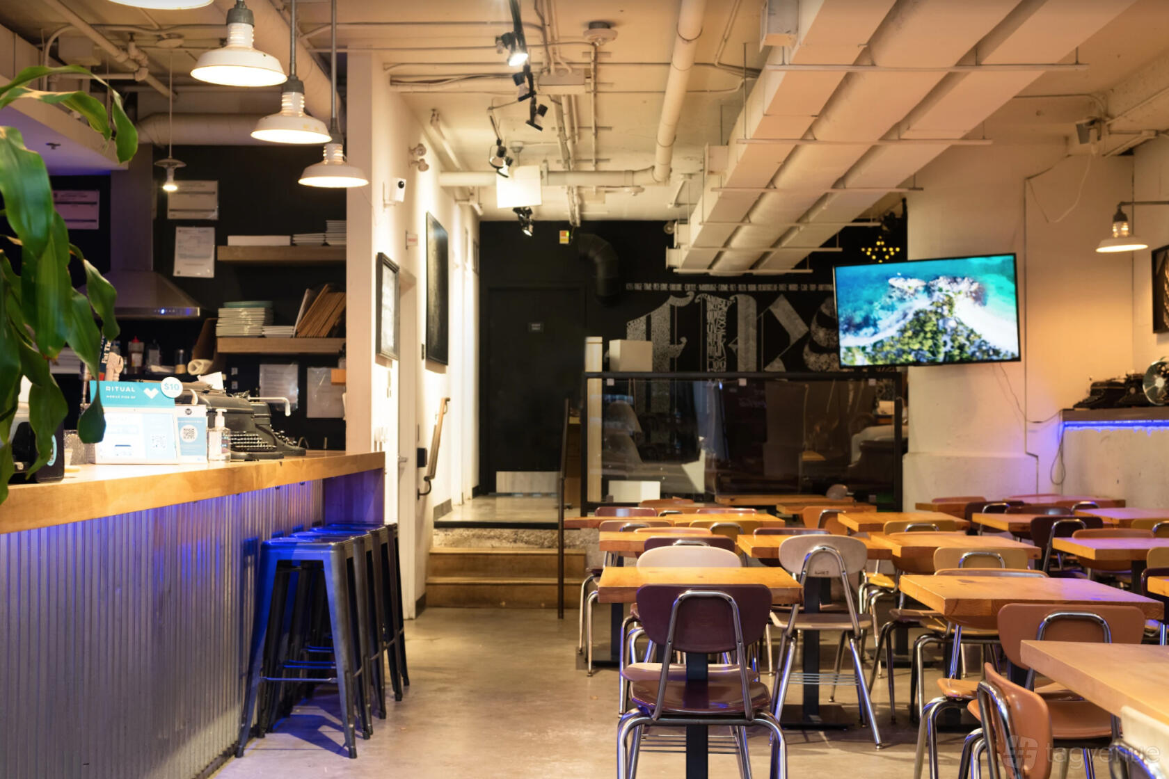 A cafe with wooden tables, metal chairs, a corrugated counter with barstools, and overhead pendant lights at Page One Cafe.