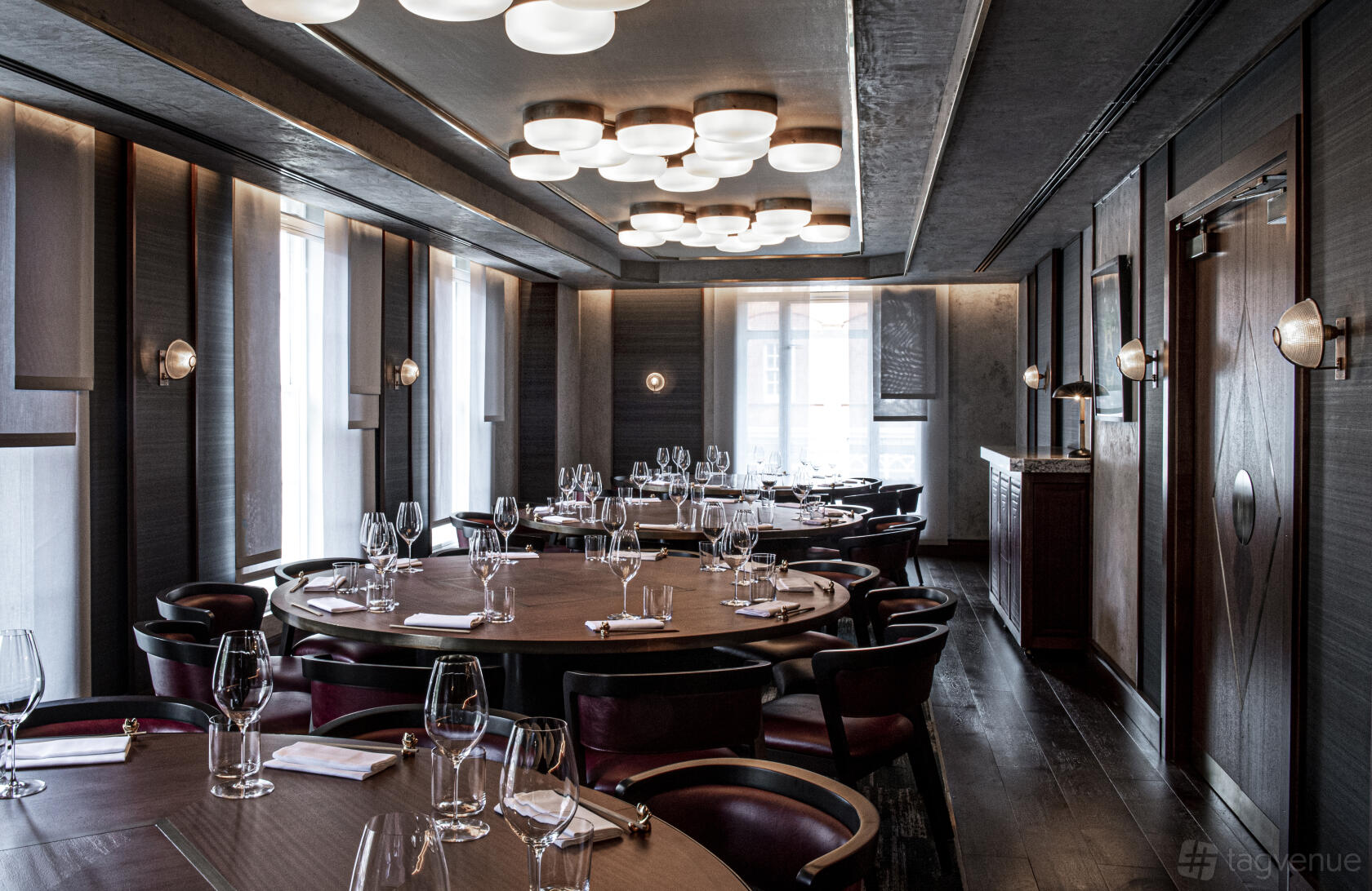 A dining room with large round tables, dark wood floors, and modern ceiling lights at Lucky Cat.