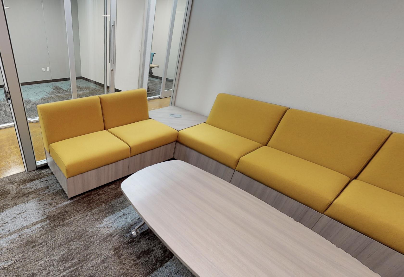 A coworking space with yellow modular sofas and a light wood coffee table at Innovation WorkSpaces.