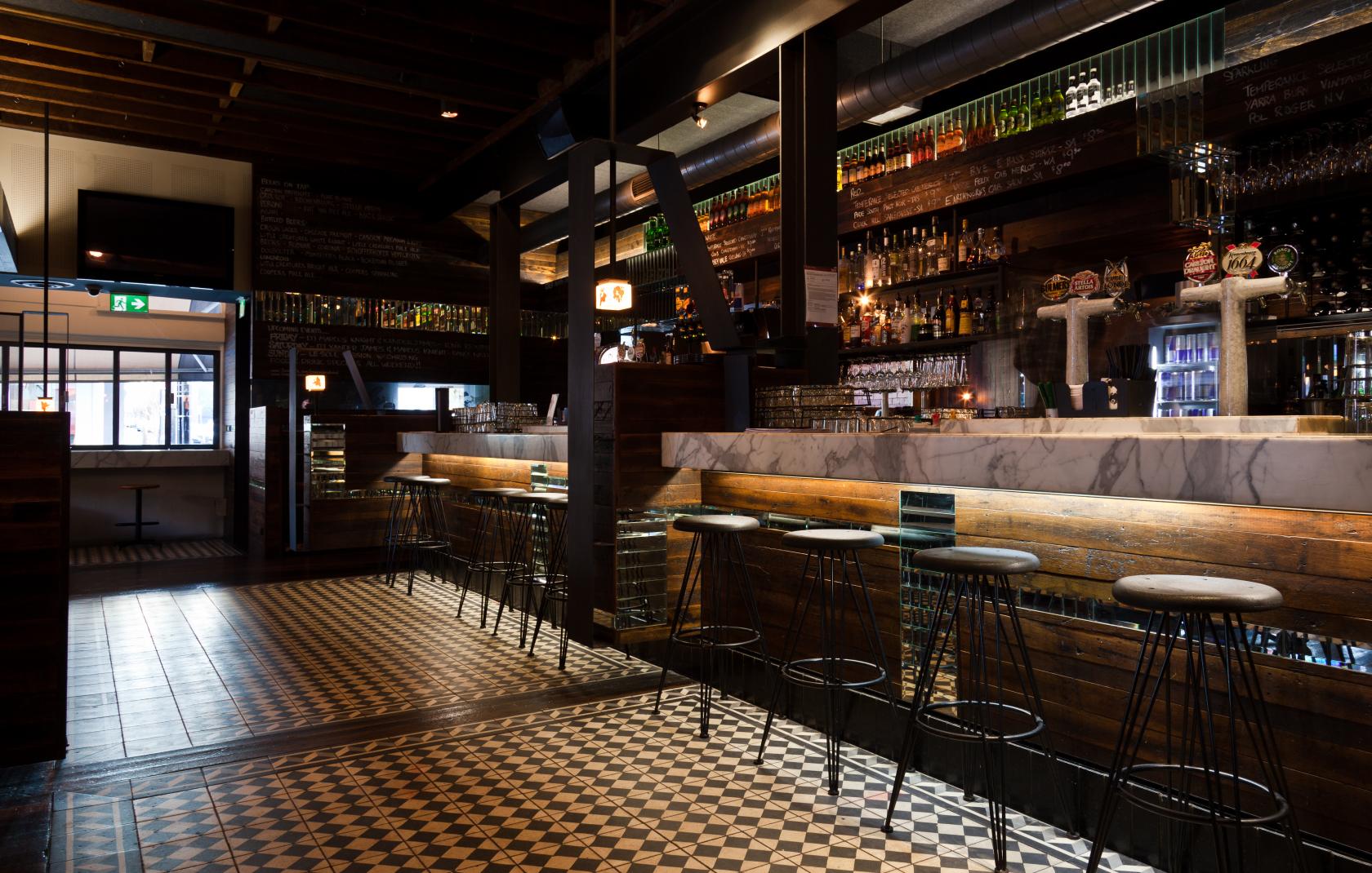 An event space in a pub with patterned tile floors, a marble bar, and shelves of liquor bottles at Temperance Hotel.