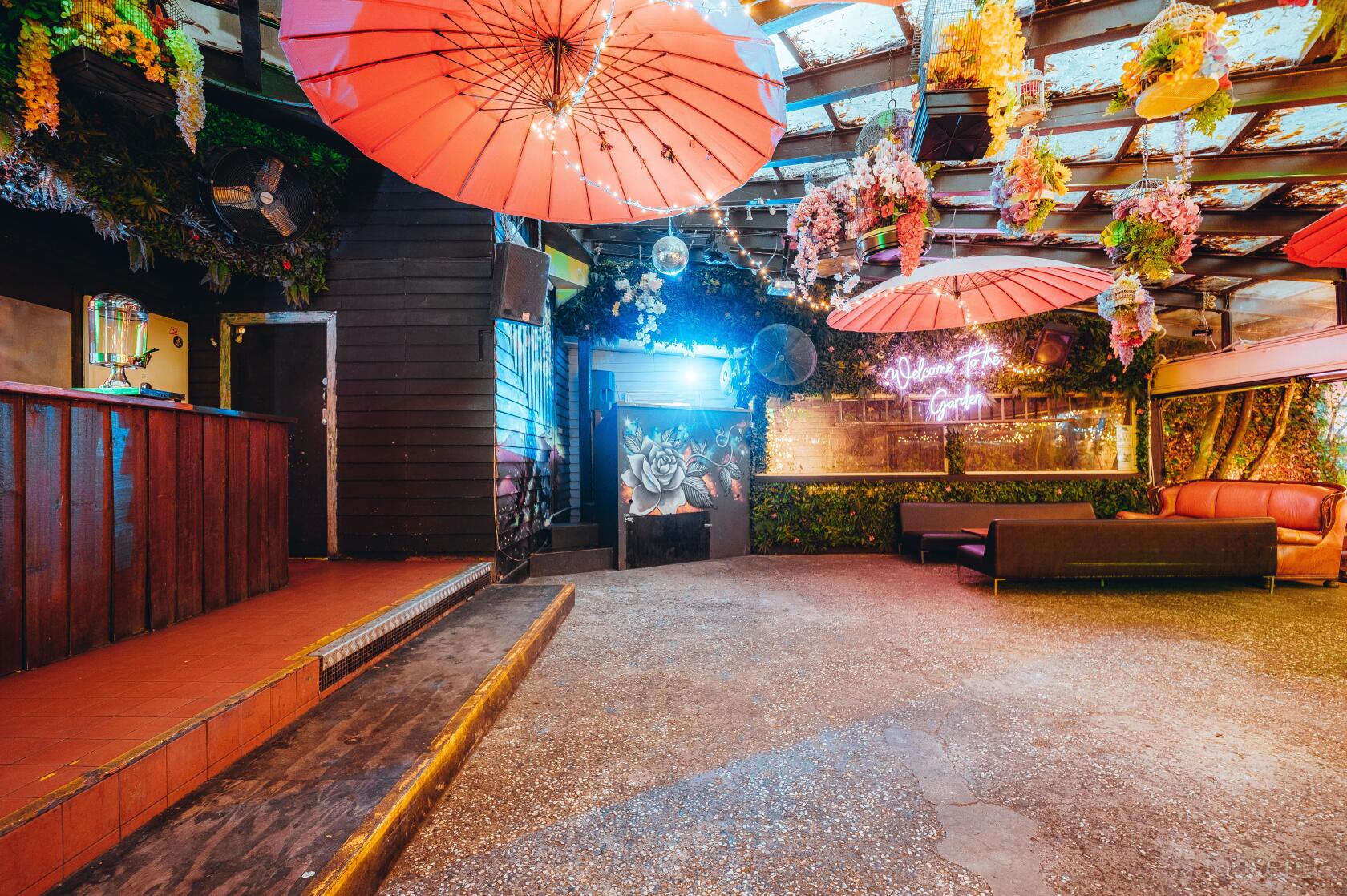 A pub with large red umbrellas, floral ceiling decor, neon signs, and lounge seating at The Fitzroy Beer Garden.