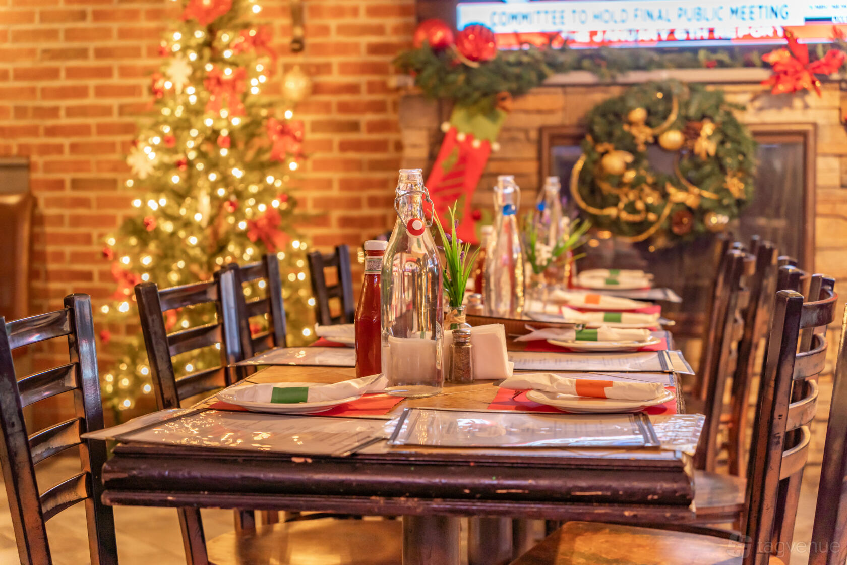 A restaurant with a decorated holiday tree, brick wall, and a long table set with water bottles at Austin's Ale House.