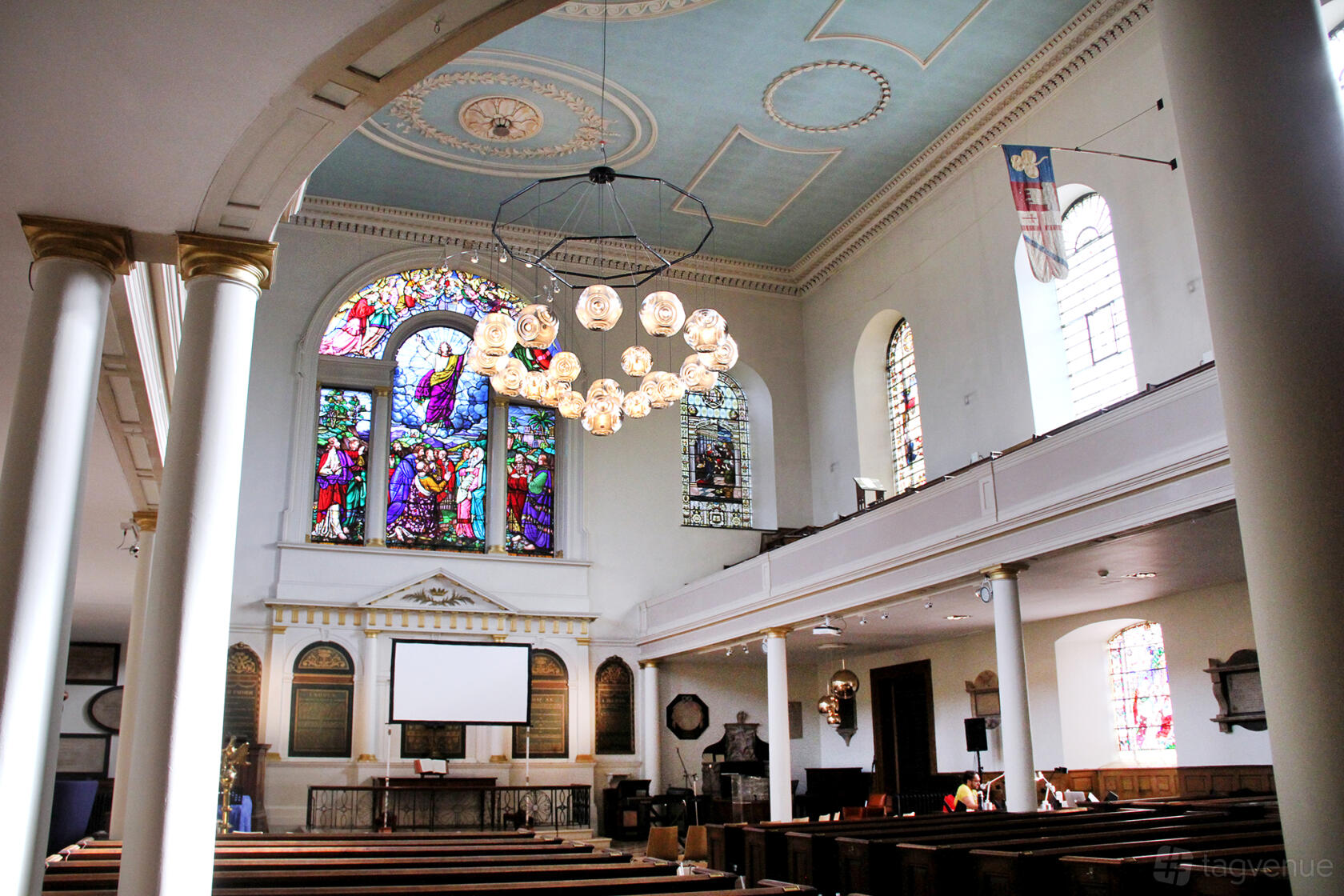 An event space in a church with stained glass windows, vaulted ceiling, wooden pews, and a modern chandelier at Crypt on the Green.