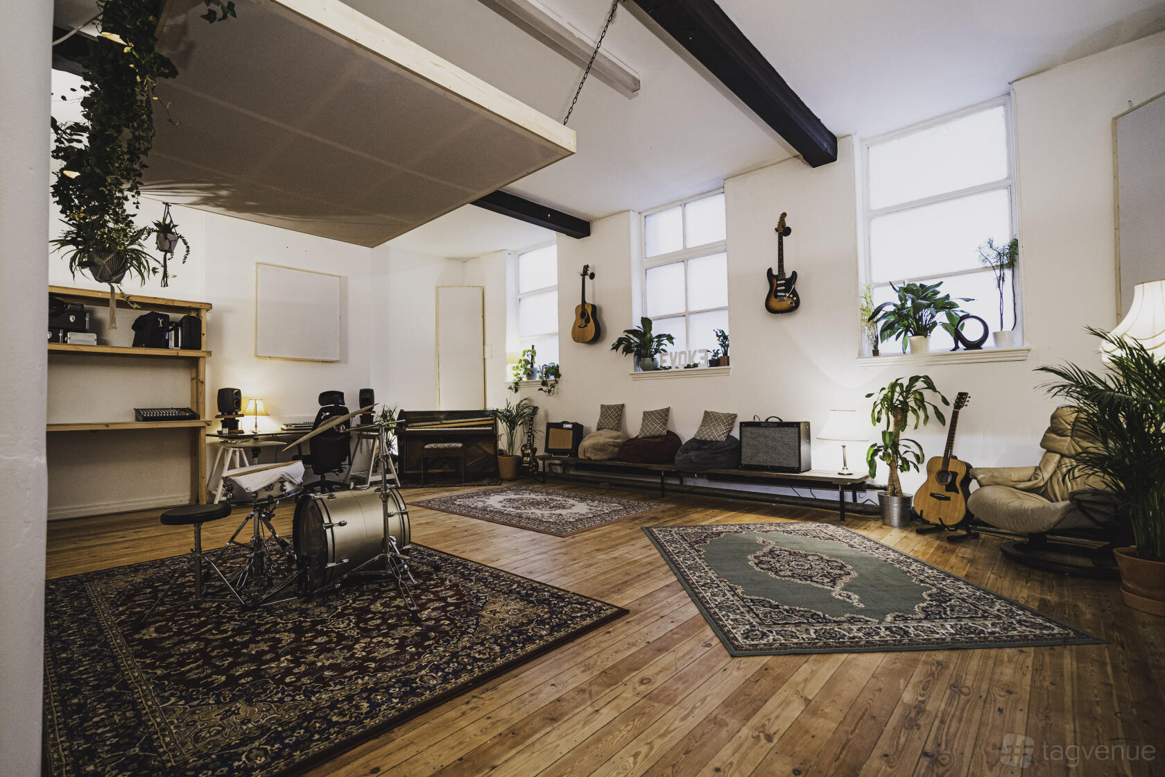 A recording studio with hardwood floors, drum set, wall-mounted guitars, and potted plants at Evoke Studios.