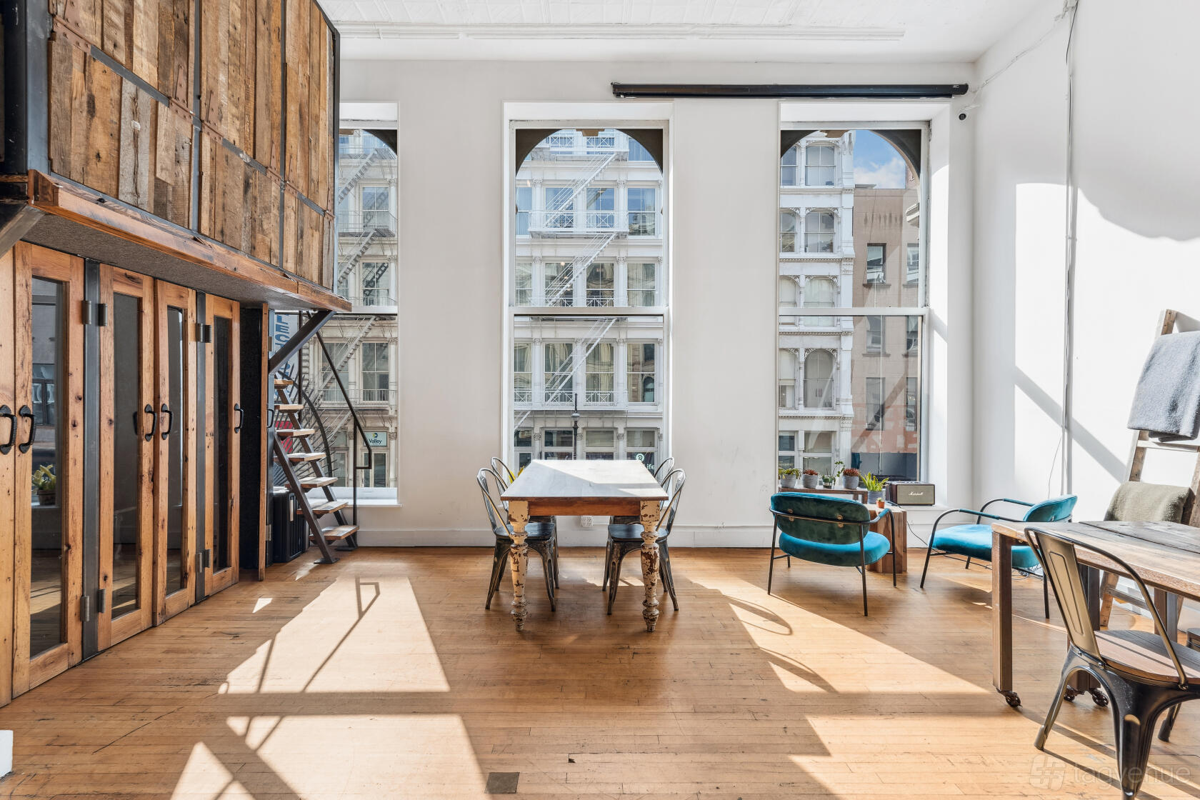 A function room with large arched windows, natural light, wood floors, and modern seating at The Farm Soho.