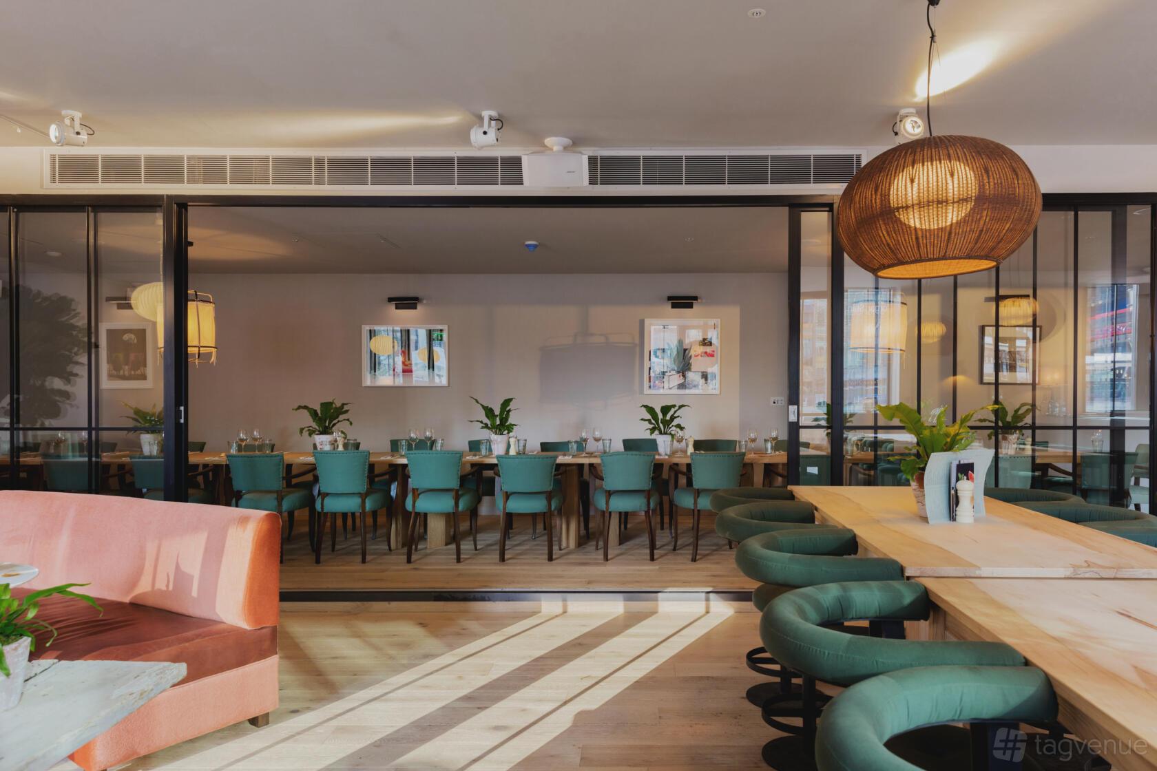 A dining room with teal upholstered chairs, wooden tables, potted plants, and pendant lighting at No.35 Mackenzie Walk.