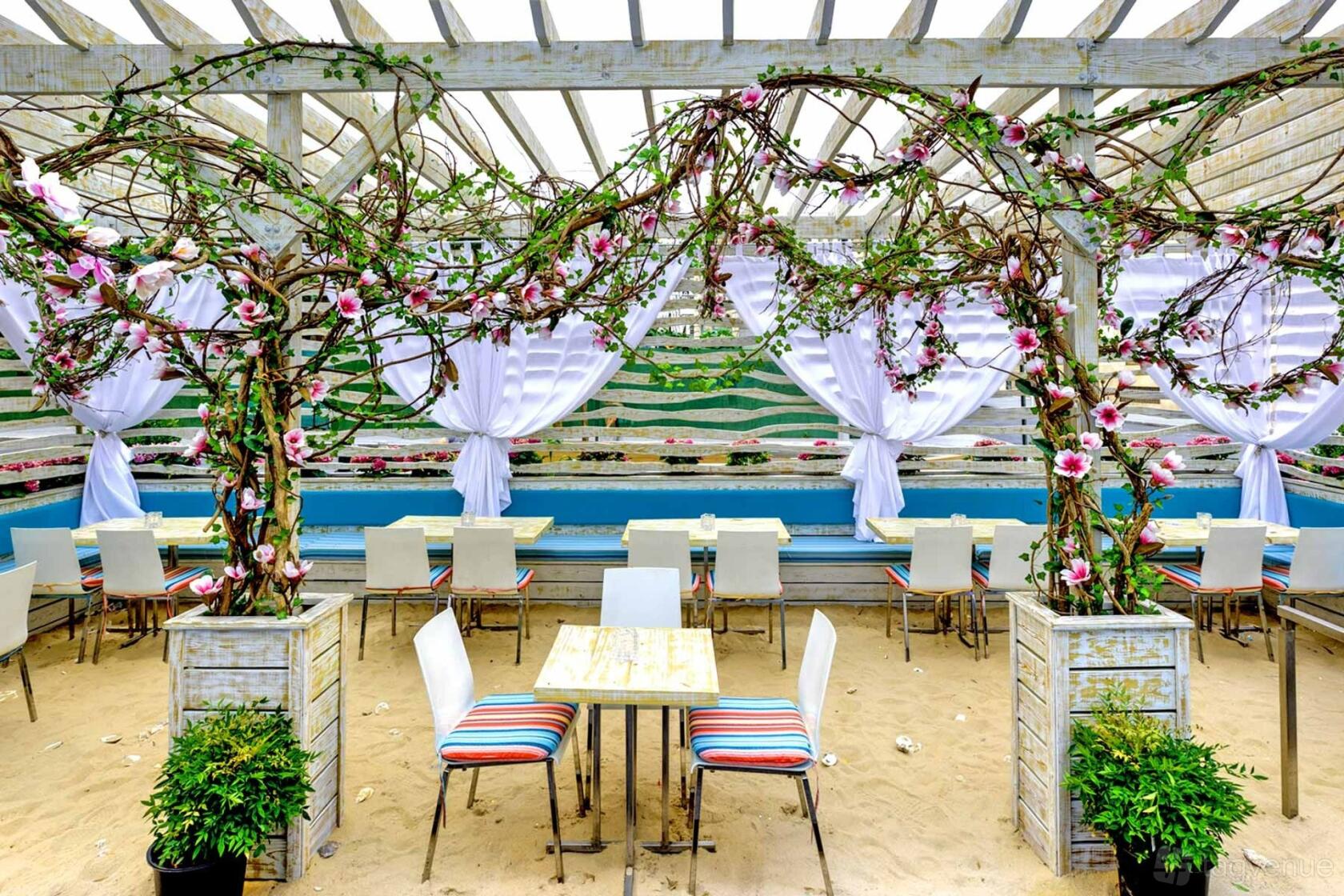 An open-air restaurant with sandy ground, floral trellises, and striped chairs under a pergola at Skinos.