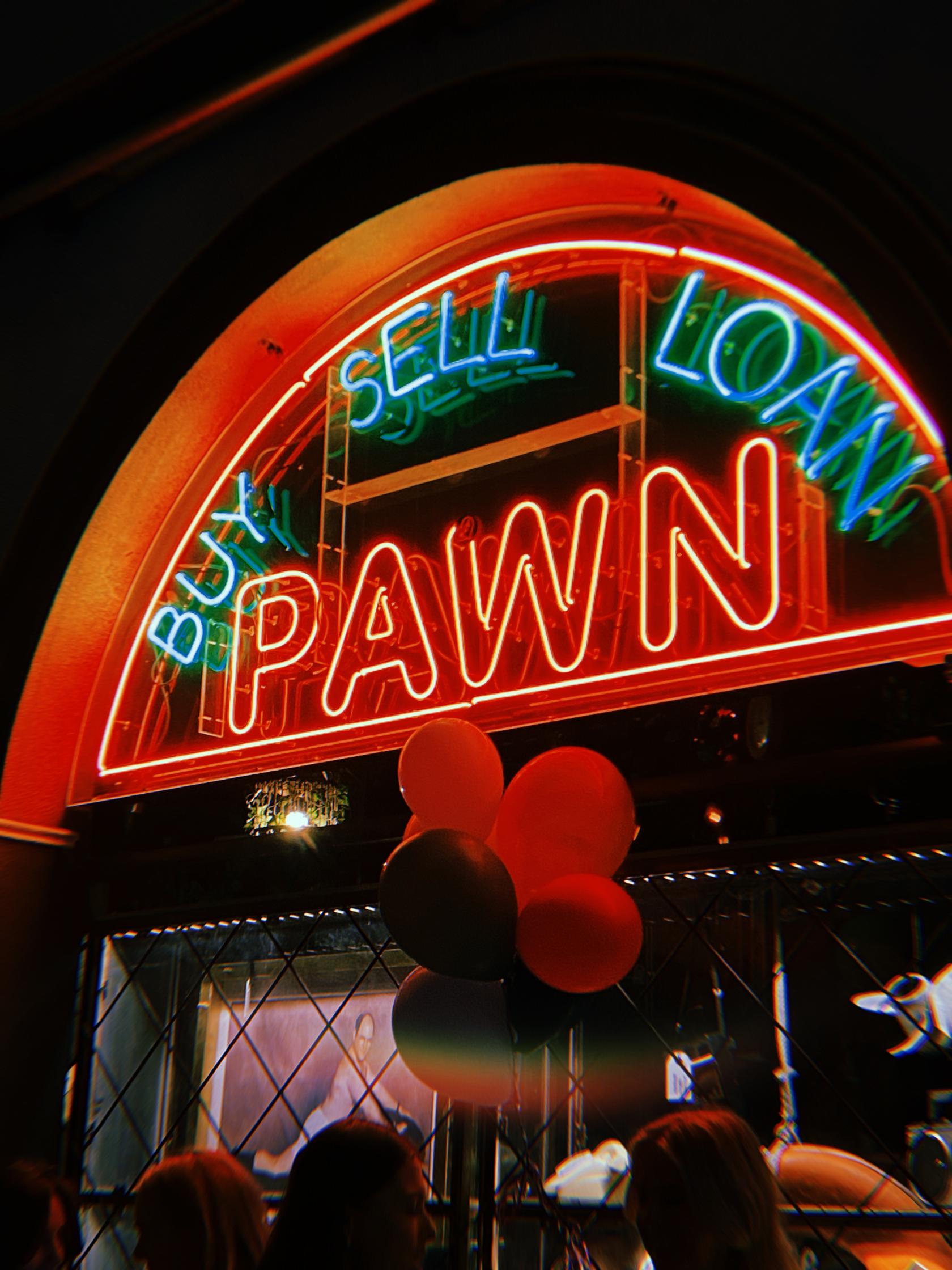 A bar entrance with neon 'BUY PAWN SELL LOAN' signage and a cluster of balloons at Pawn & Co.