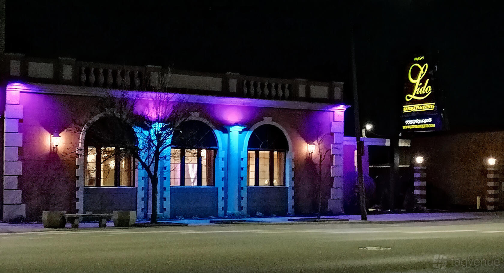 A restaurant with arched windows illuminated by colorful lights and a lit sign at Lido Banquet Hall.