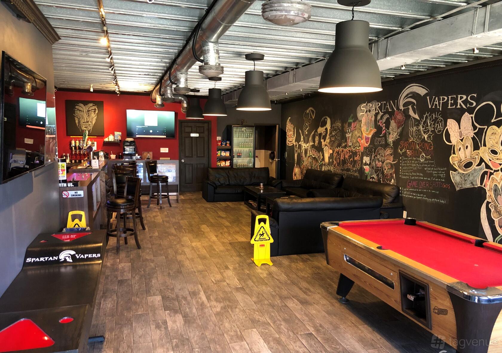 A bar with a red accent wall, black leather sofas, chalkboard mural, and a red pool table at Spartan Bar and Lounge Event Space.