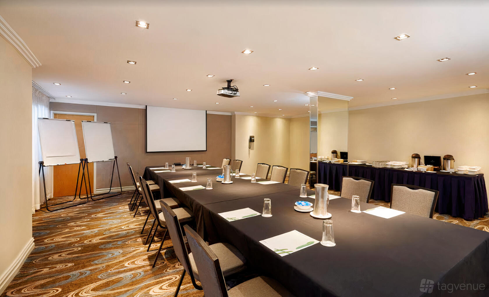 A meeting room with U-shaped tables, a projector, flip charts, and a buffet setup at Holiday Inn Parramatta.