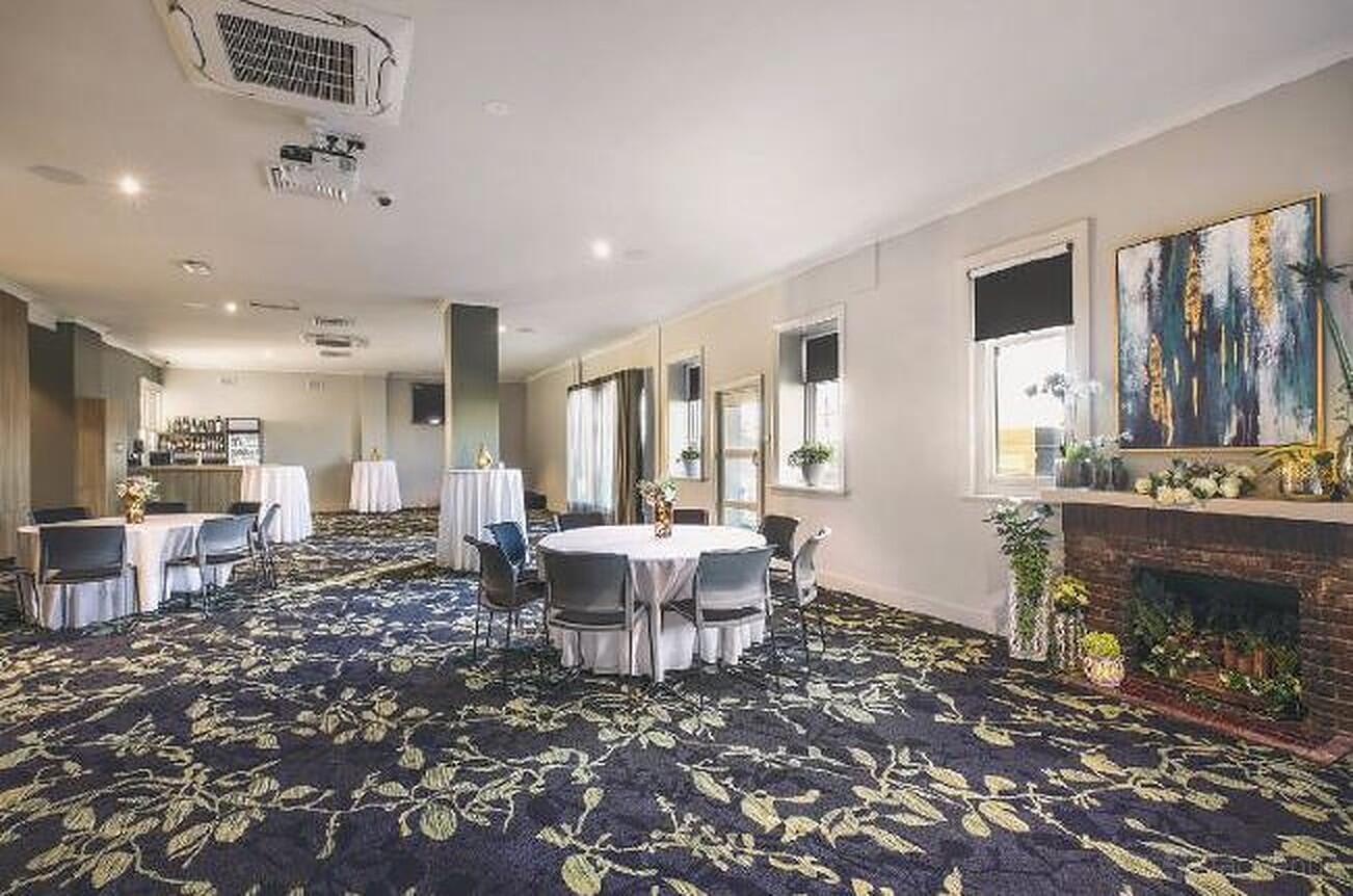 A pub function room with round tables, floral carpet, a fireplace, and a small bar at First & Last Hotel.