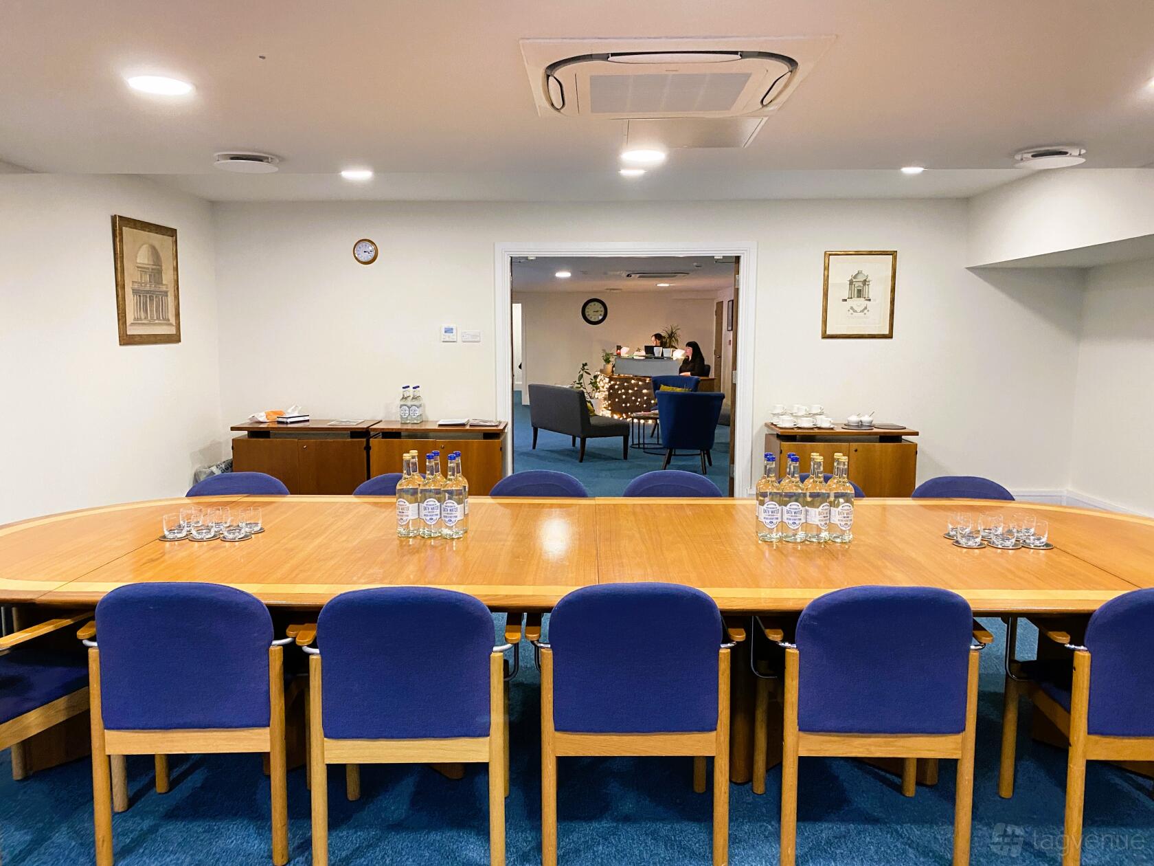 A meeting room with a large wooden boardroom table, blue chairs, and bottled water at Inigo Business Centres Bath.