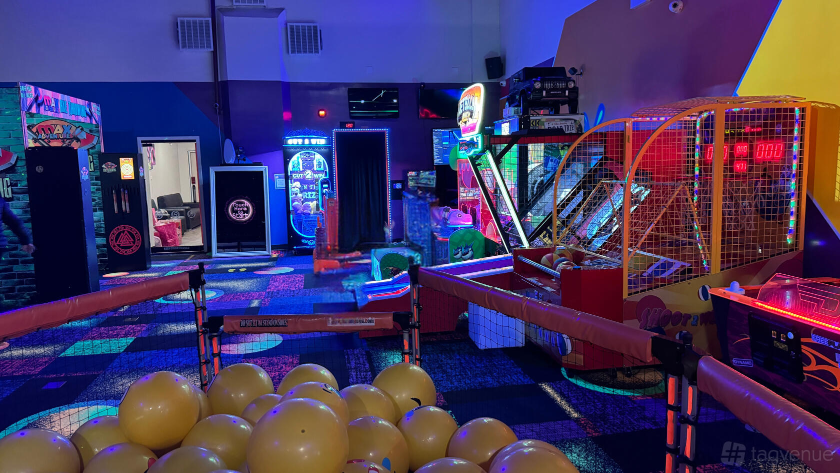 An indoor event venue with arcade games, neon lighting, and yellow play balls at Max Adventures.