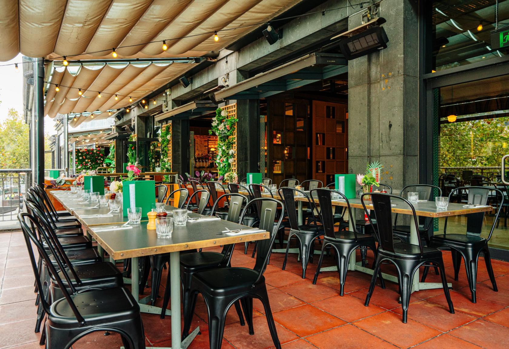 An outdoor dining area with long tables, black chairs, and a retractable awning at Hophaus.