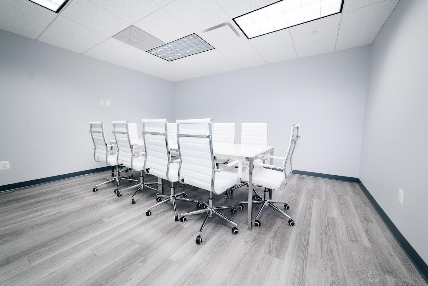 A meeting centre with a long white conference table and white leather chairs on wood flooring at Perfect Office Solutions - Rockville.