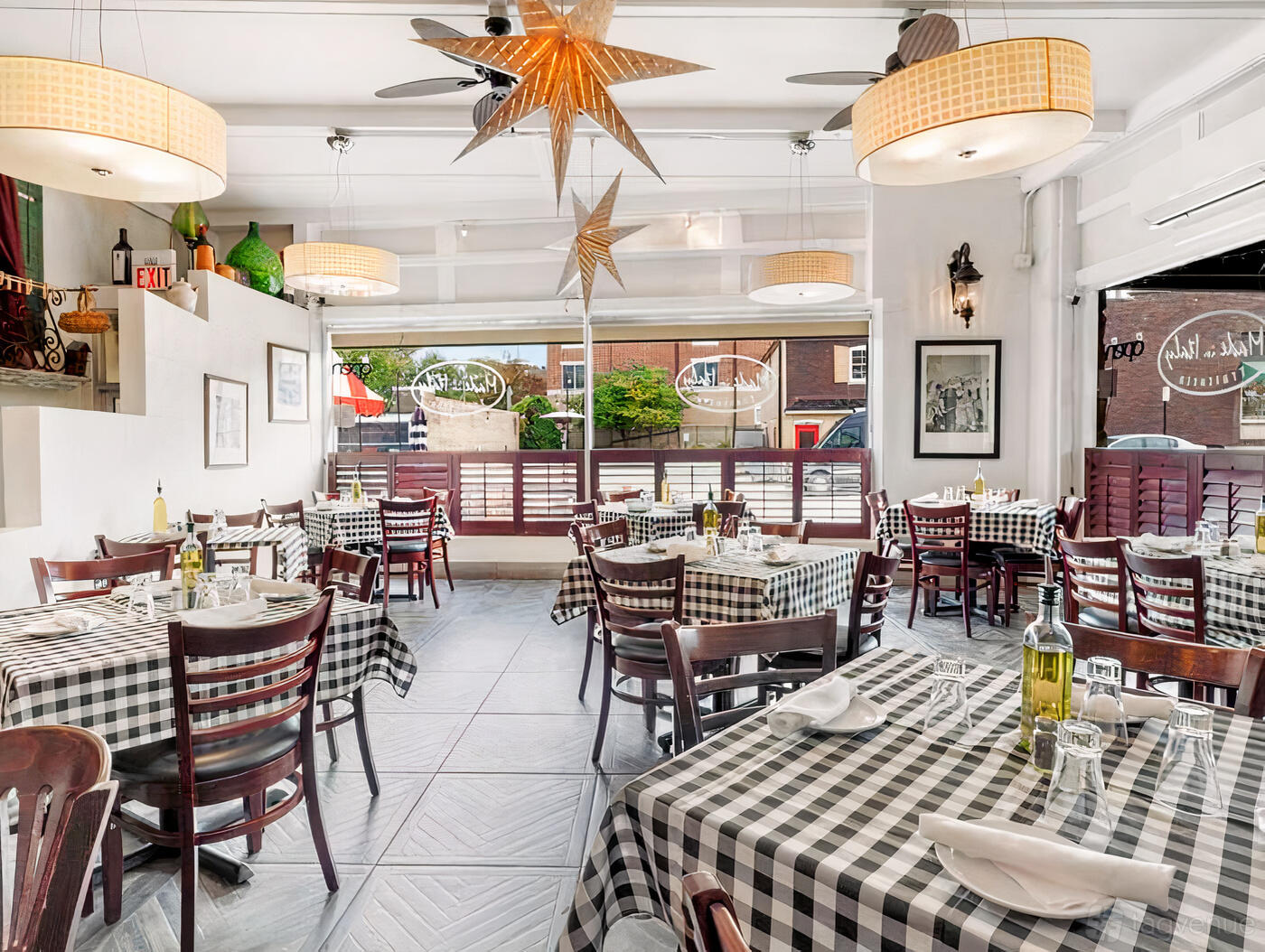 A restaurant with checkered tablecloths, wooden chairs, large windows, and hanging star lamps at Made in Italy Trattoria.