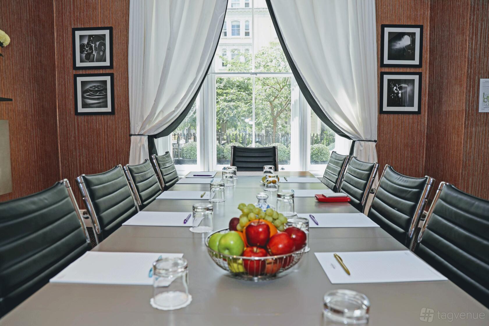 A hotel event space with a boardroom table, leather chairs, large window, and natural light at Mercure London Hyde Park.