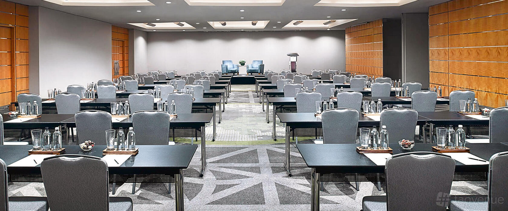 A hotel ballroom with conference tables arranged classroom-style, grey chairs, and ceiling lights at Pan Pacific Singapore.