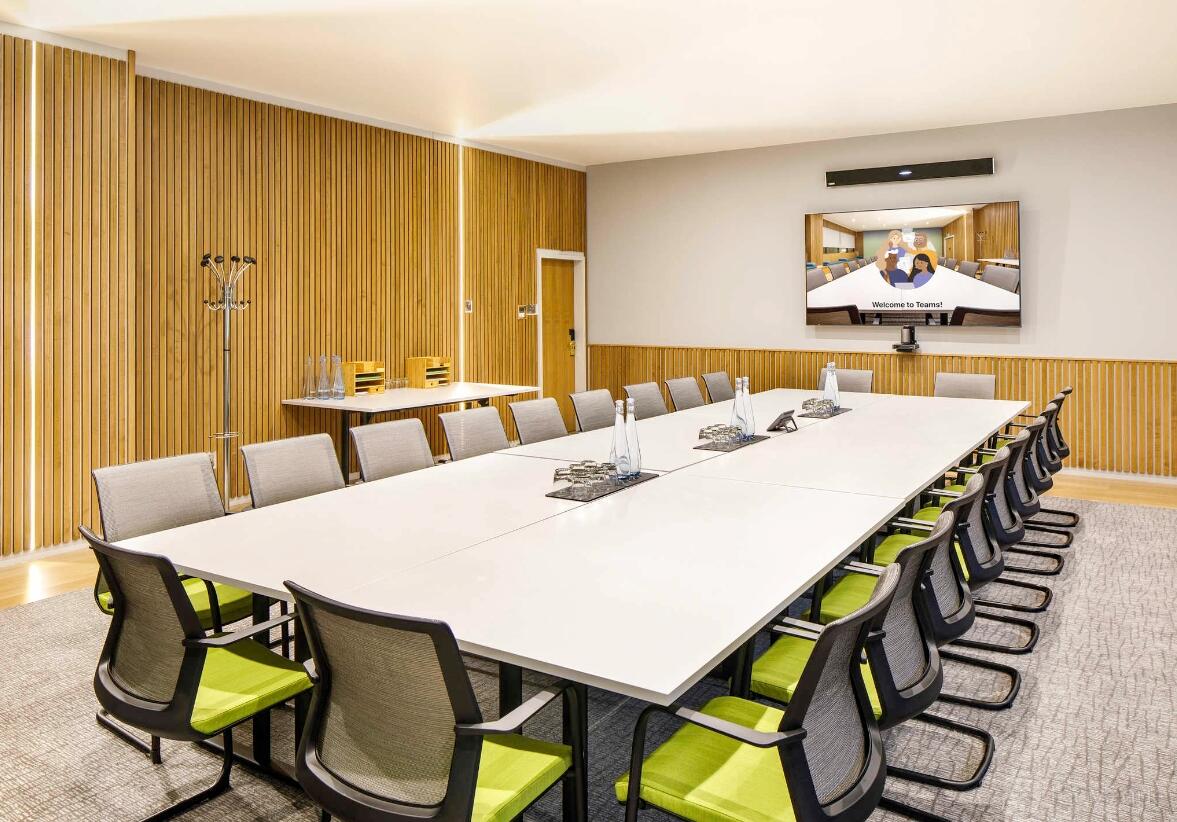 A meeting room with a long conference table, ergonomic chairs, and wood panel walls at Mercure Bedford Centre.