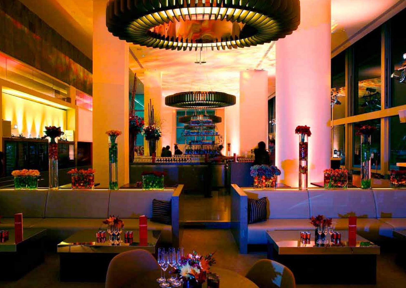 A restaurant with colorful mood lighting, floral centerpieces, and large circular chandeliers at Skylon.