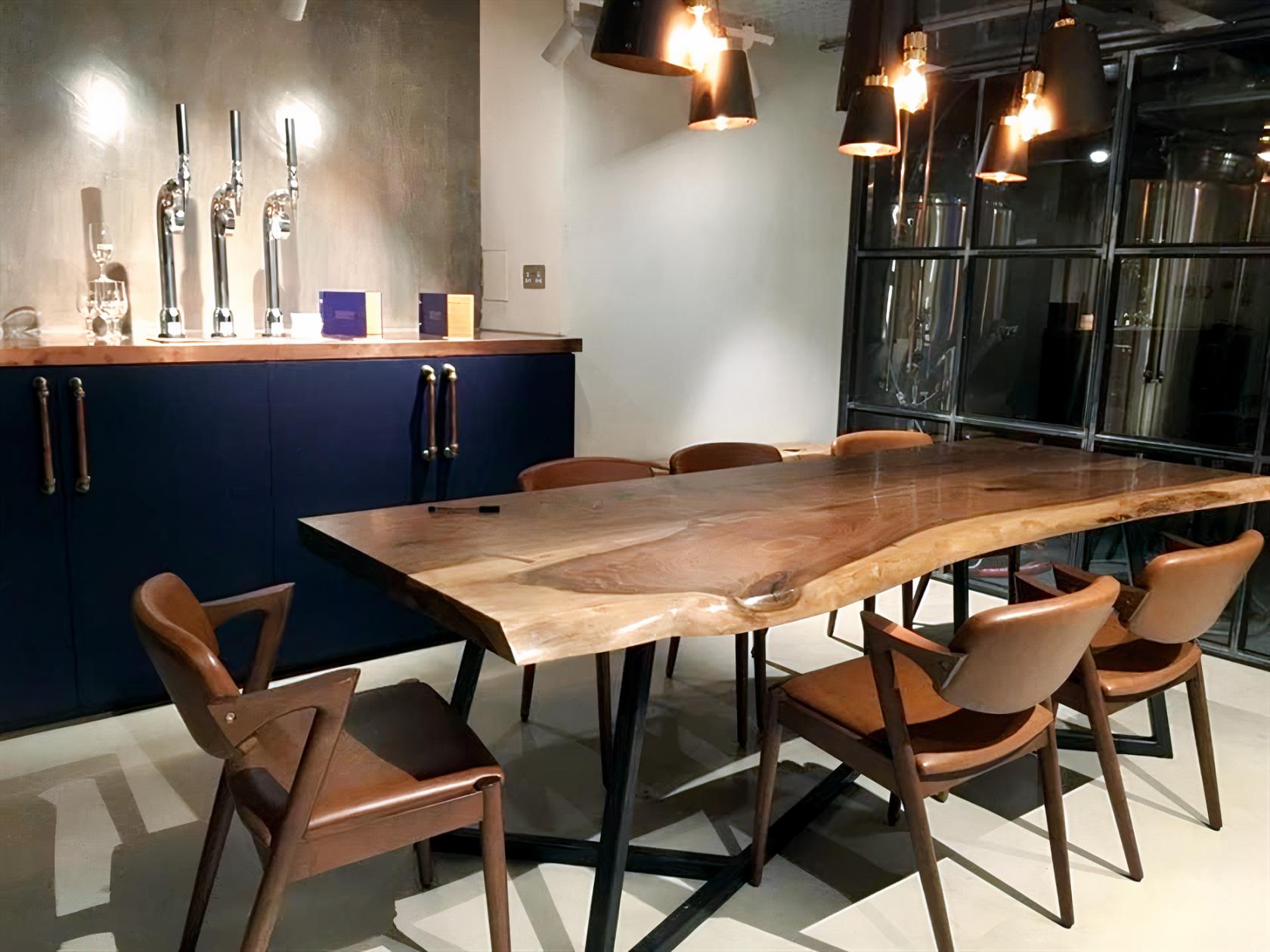 An event space with a live edge wooden table, leather chairs, hanging lights, and visible brewery tanks at Shilling Brewing Company.