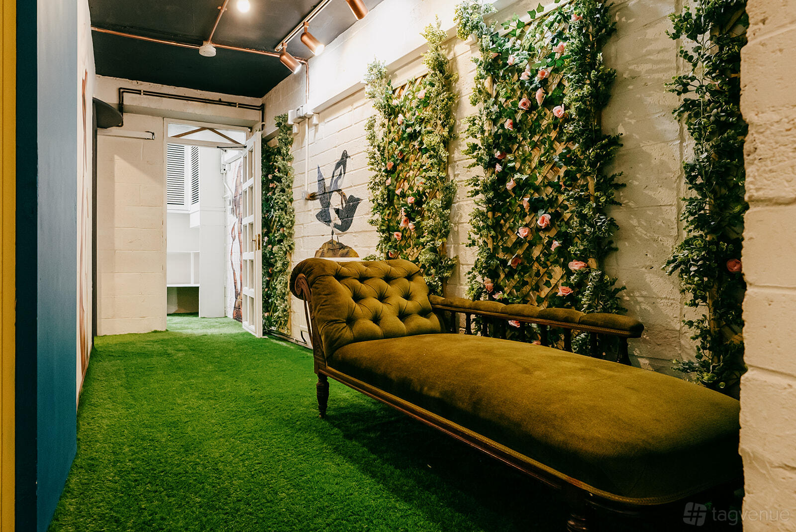 An event venue with a green velvet chaise lounge and floral trellis walls on artificial grass at Blake 1757.