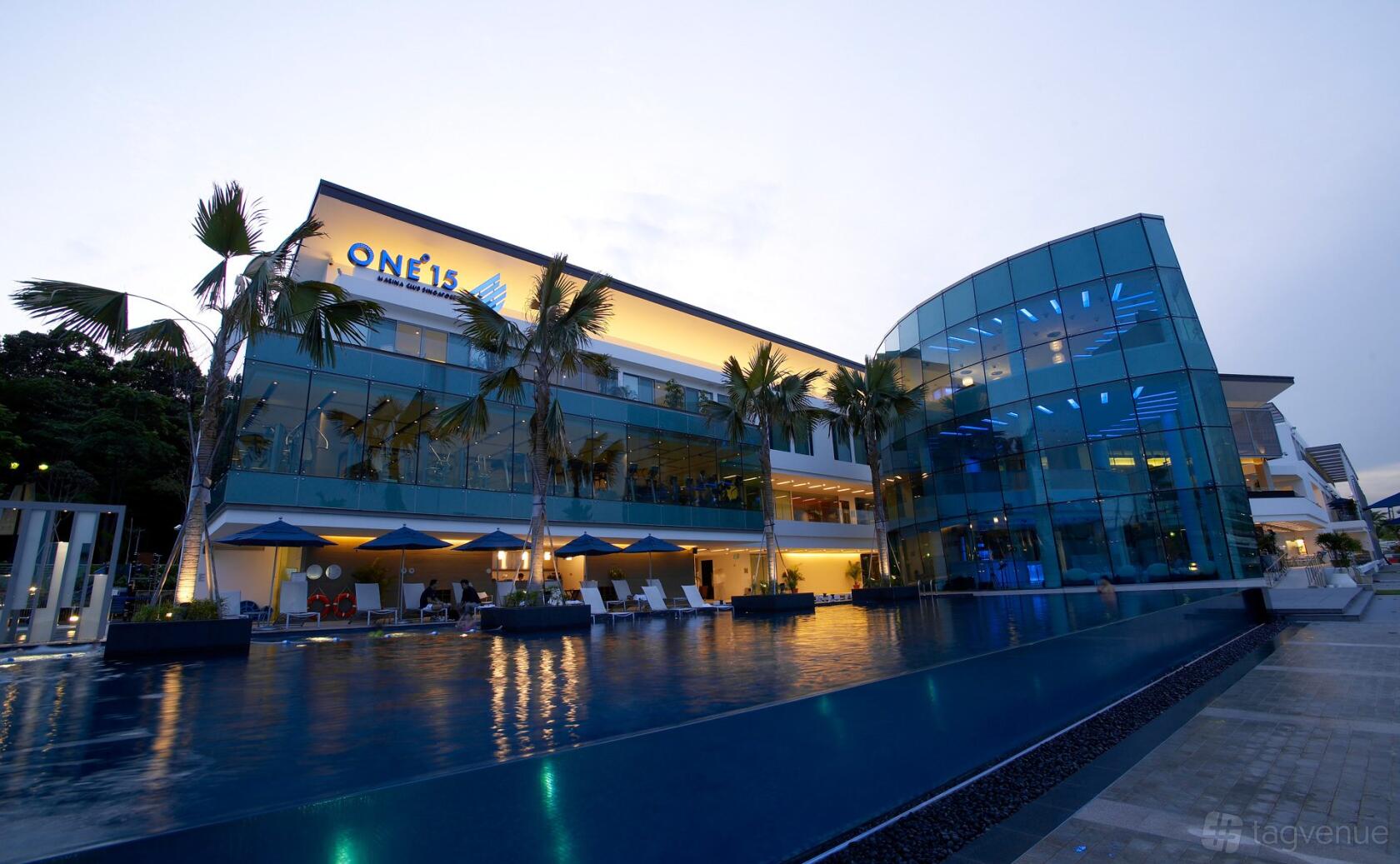 A hotel with a glass façade, palm trees, and an outdoor swimming pool at ONE°15 Marina Sentosa Cove.