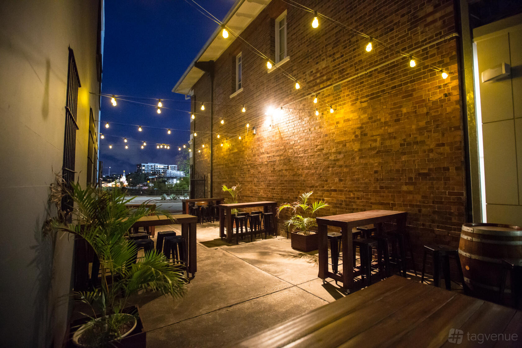 An outdoor terrace with string lights, brick walls, tall wooden tables, and potted plants at The Mix Bar.