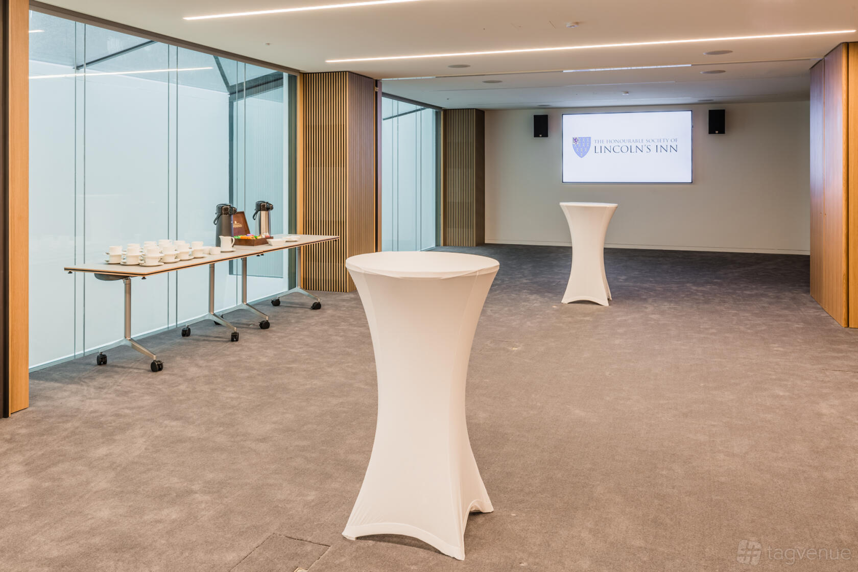 A theatre with glass walls, grey carpet, and high tables with white covers at The Honourable Society of Lincoln's Inn.