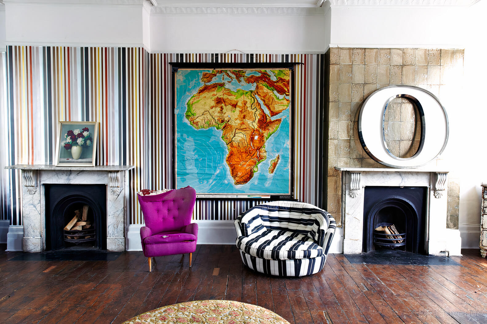 An event venue with striped wallpaper, marble fireplaces, eclectic seating, and a colorful map of Africa at The Roost.