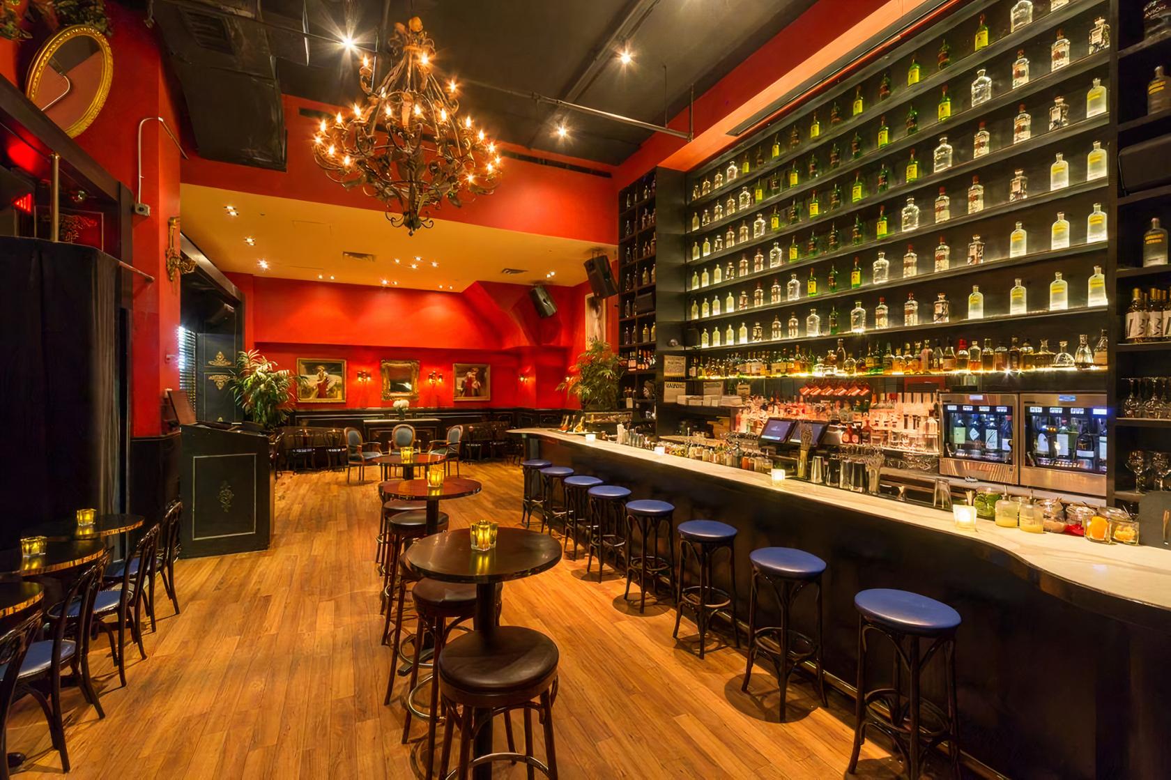 A bar with a long marble counter, high shelves of liquor, wood floors, and a chandelier at Lea Wine Bar & Lounge.