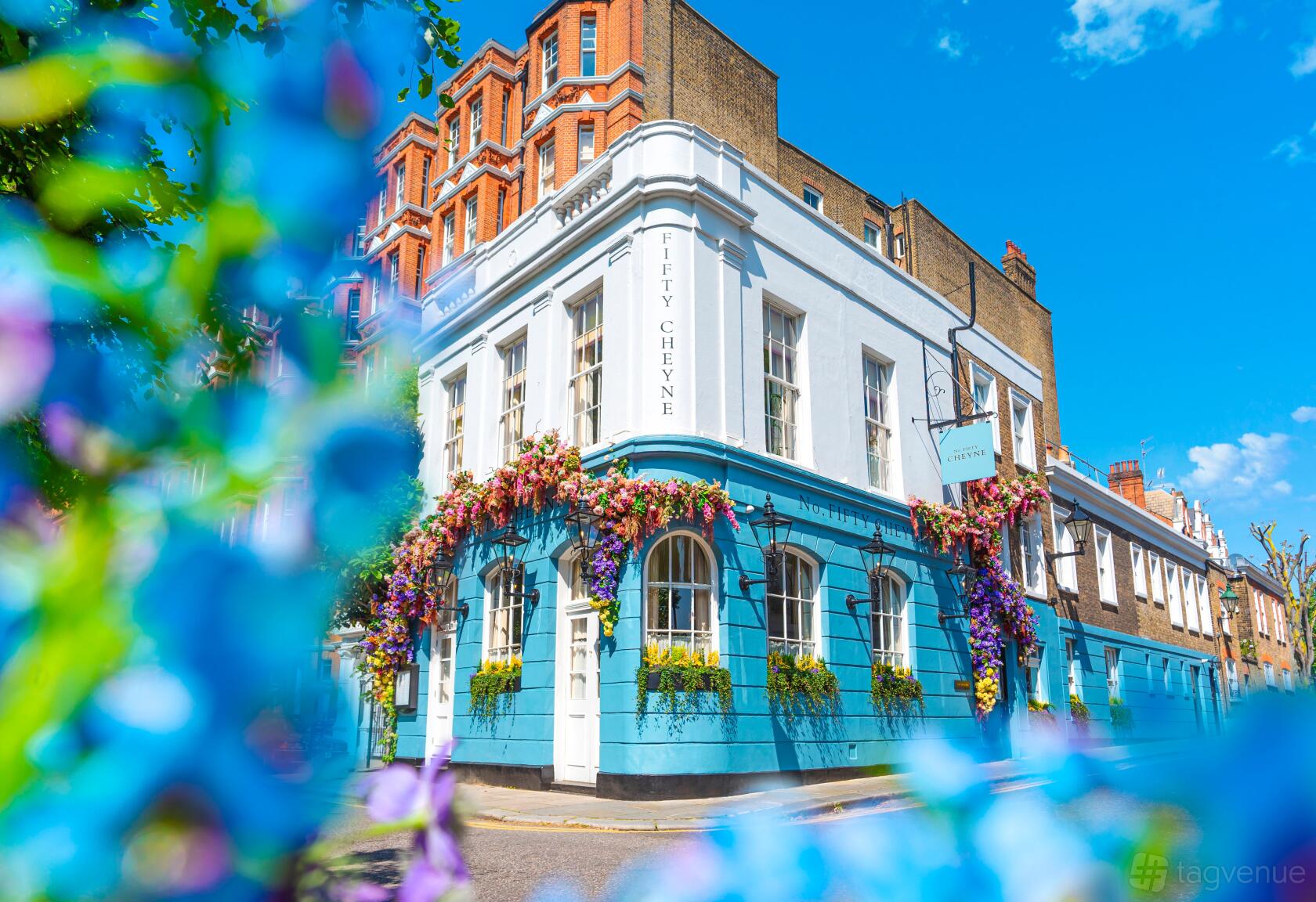 A restaurant with a blue and white exterior, floral window boxes, and street corner location at No. Fifty Cheyne.