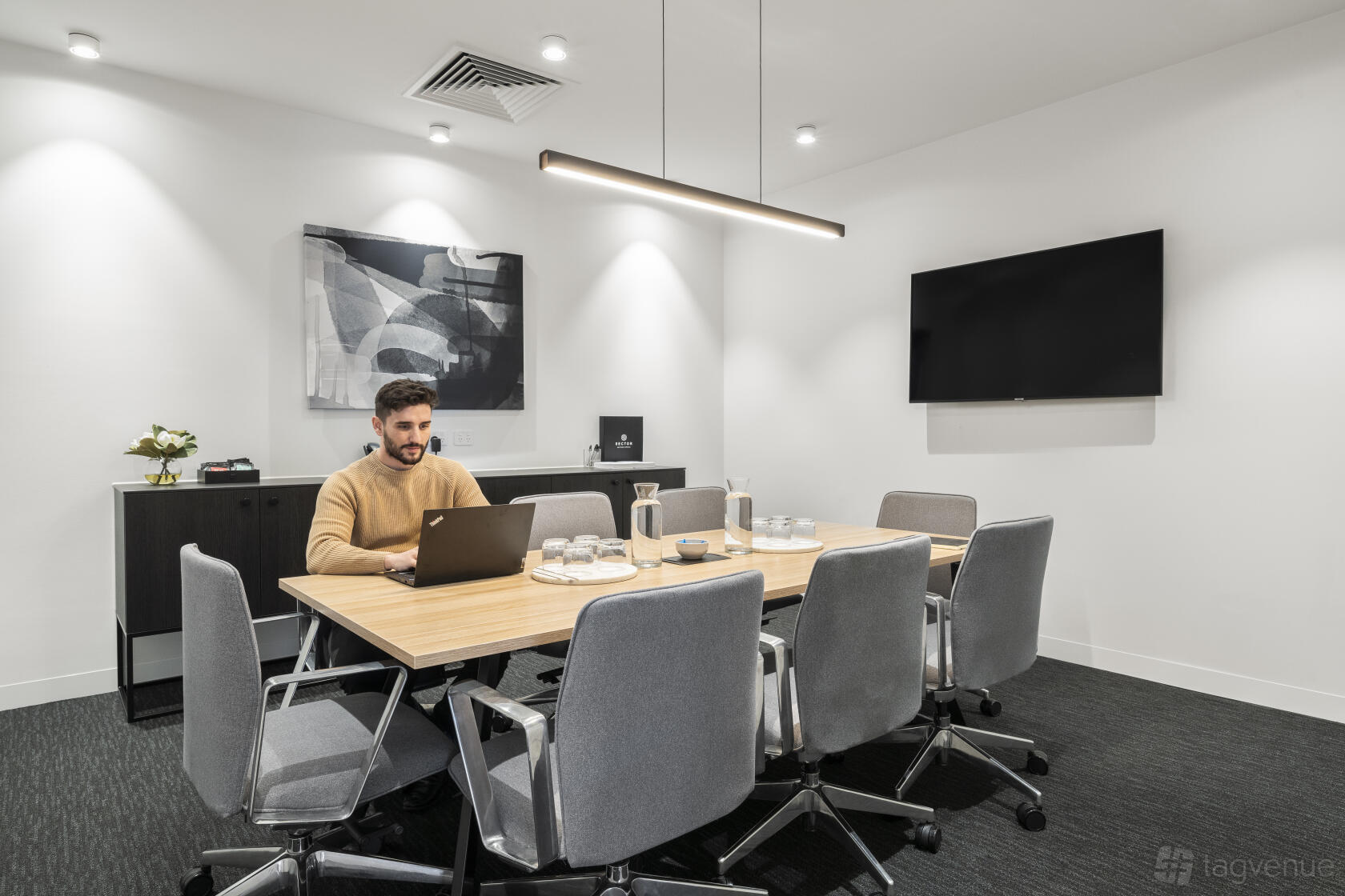 A meeting room with a wooden conference table, grey swivel chairs, wall-mounted TV, and modern artwork at Sector Serviced Offices - Clayton.