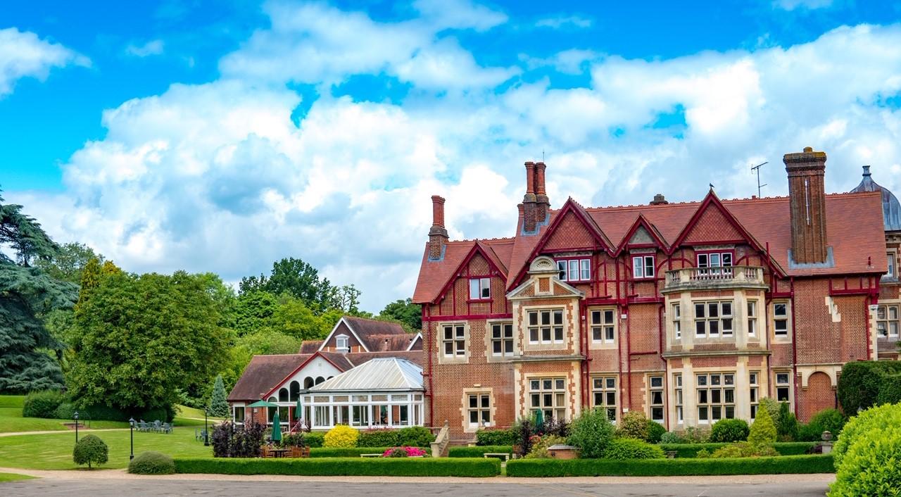 A historic hotel with red gabled roofs, large chimneys, and manicured gardens at Pendley Manor Hotel.