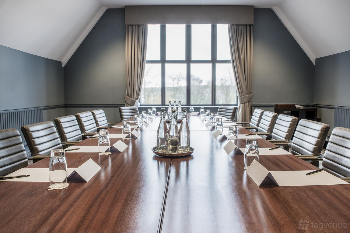 A hotel meeting room with a long wooden boardroom table, leather chairs, and large windows at Voco Oxford Spires.