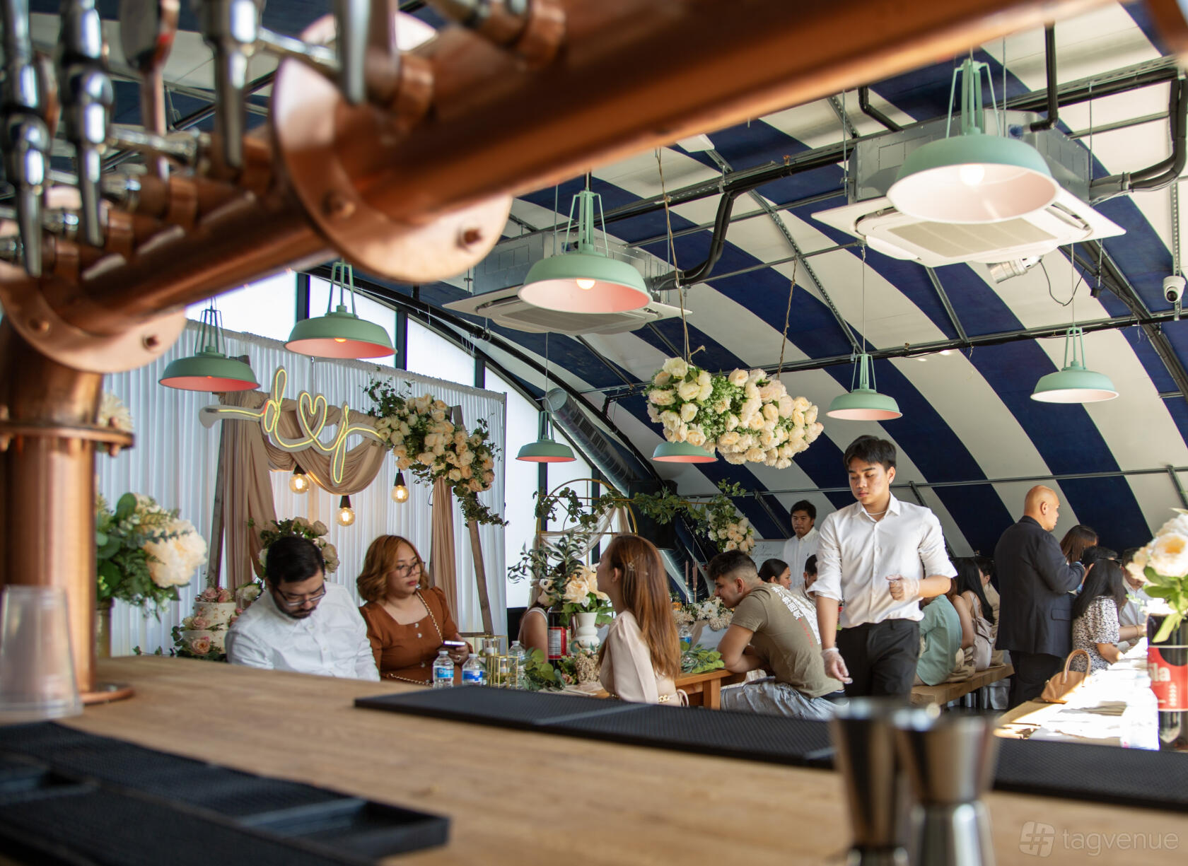 An event space in a brewery with striped ceiling, pendant lighting, and floral decorations at 3Locks Industrial Brewery Riverside Views.