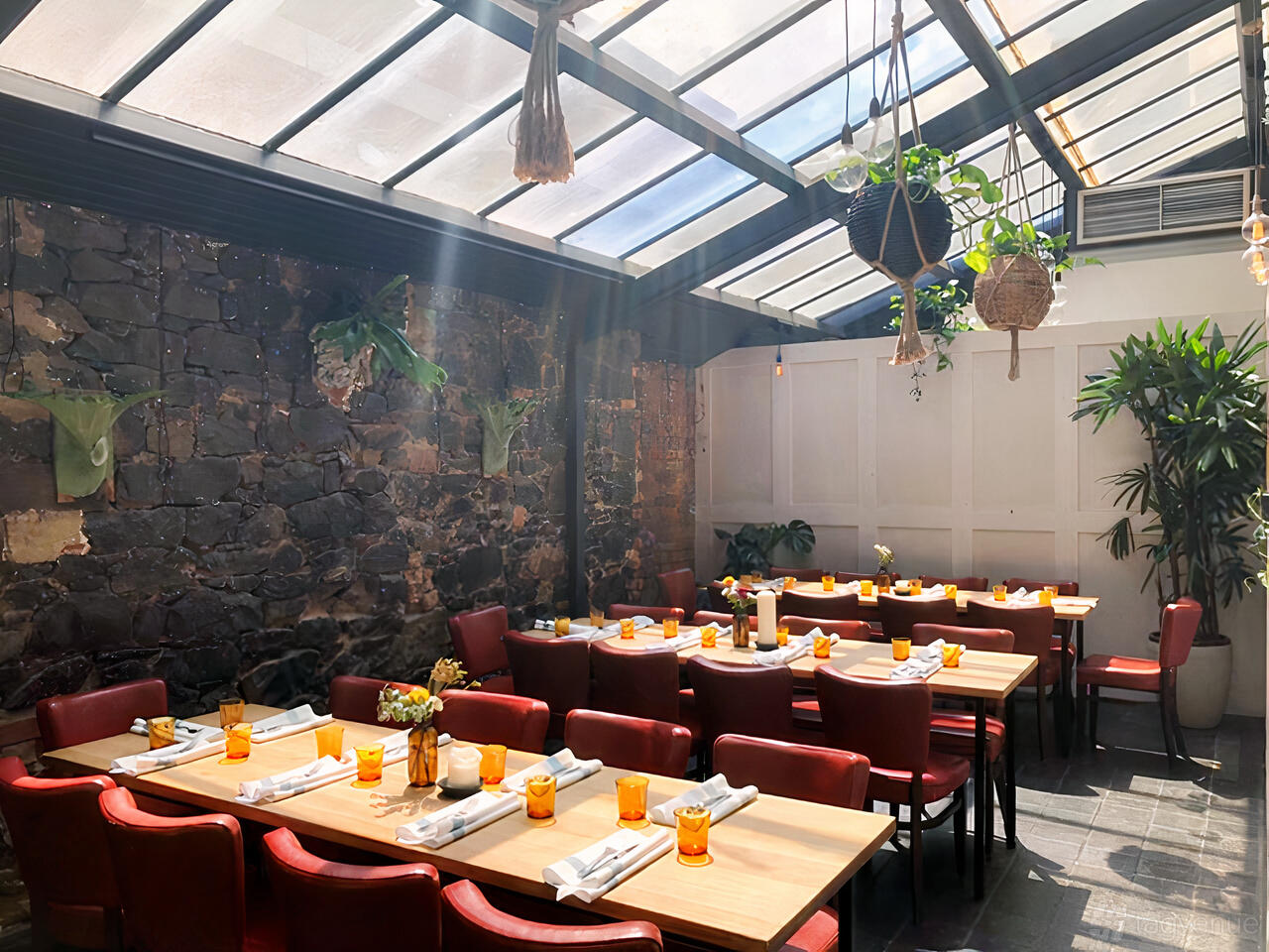 An event space with exposed stone walls, red chairs, skylights, and hanging plants at The Grace Darling Hotel.