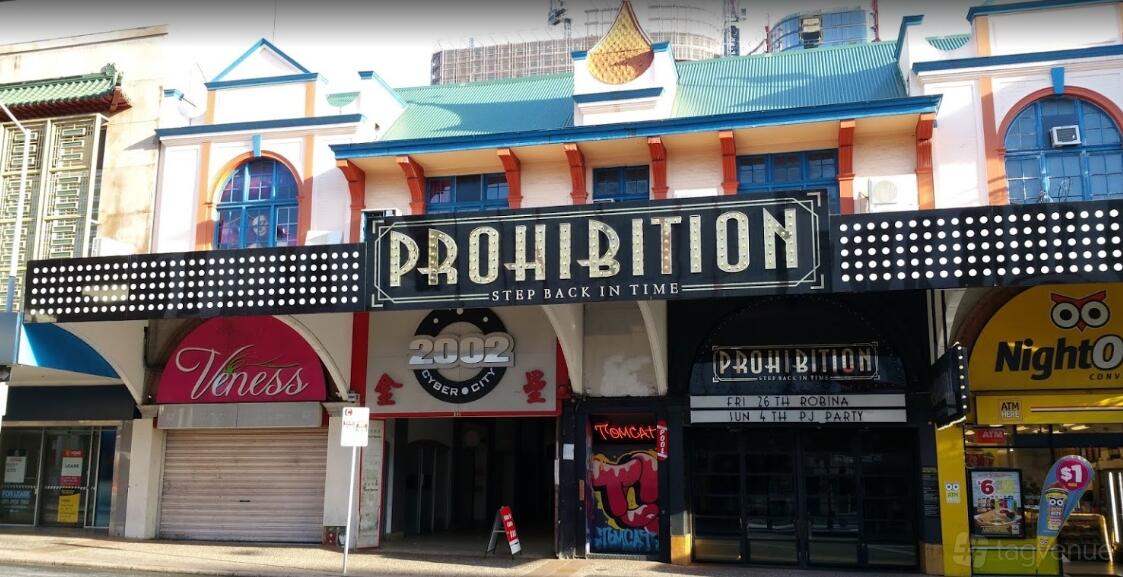 A bar with an art deco facade, bold marquee signage, and colorful storefronts at Prohibition.
