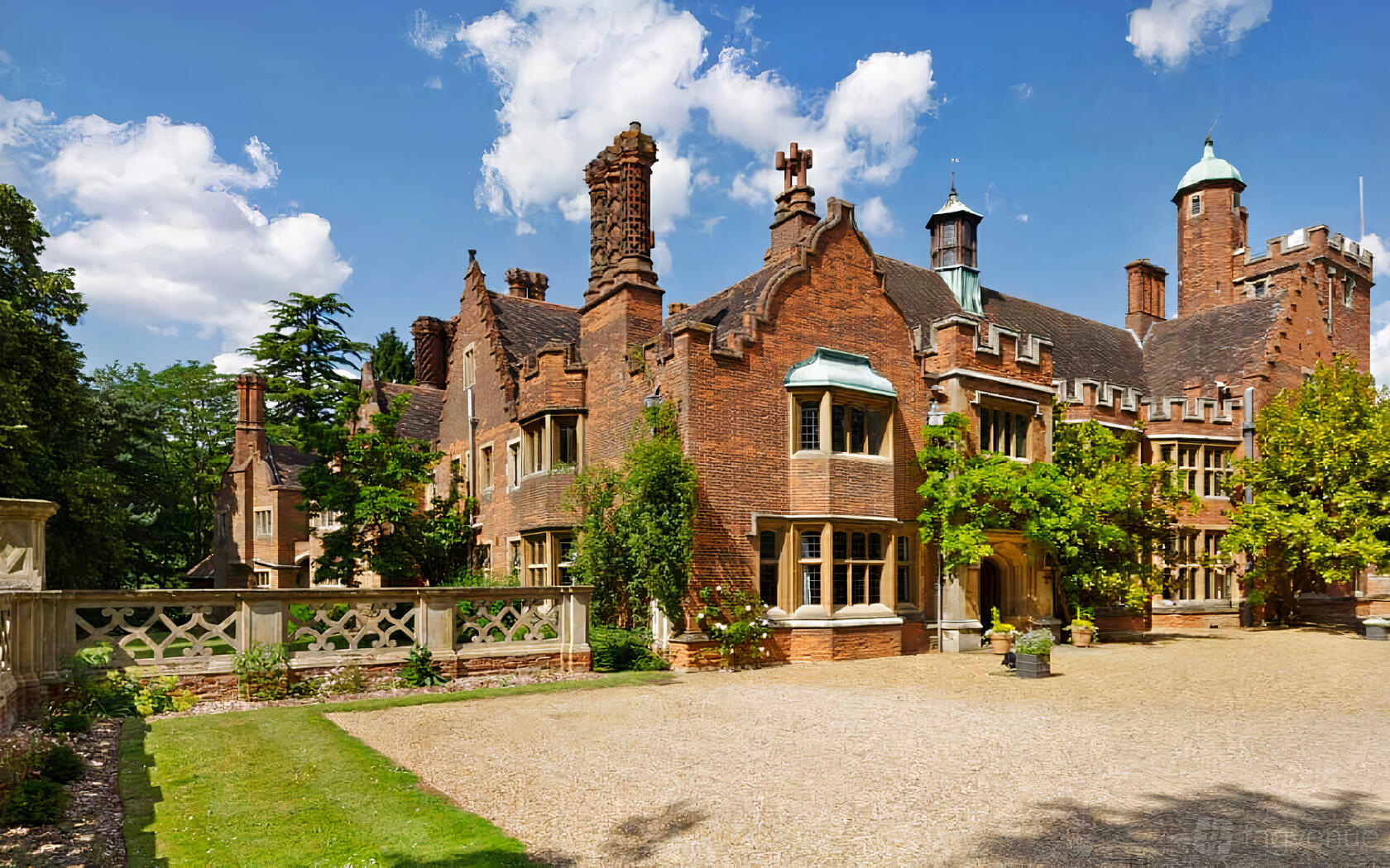 An English manor hall with red brick exterior, ornate chimneys, and stone courtyard at Lanwades Hall.