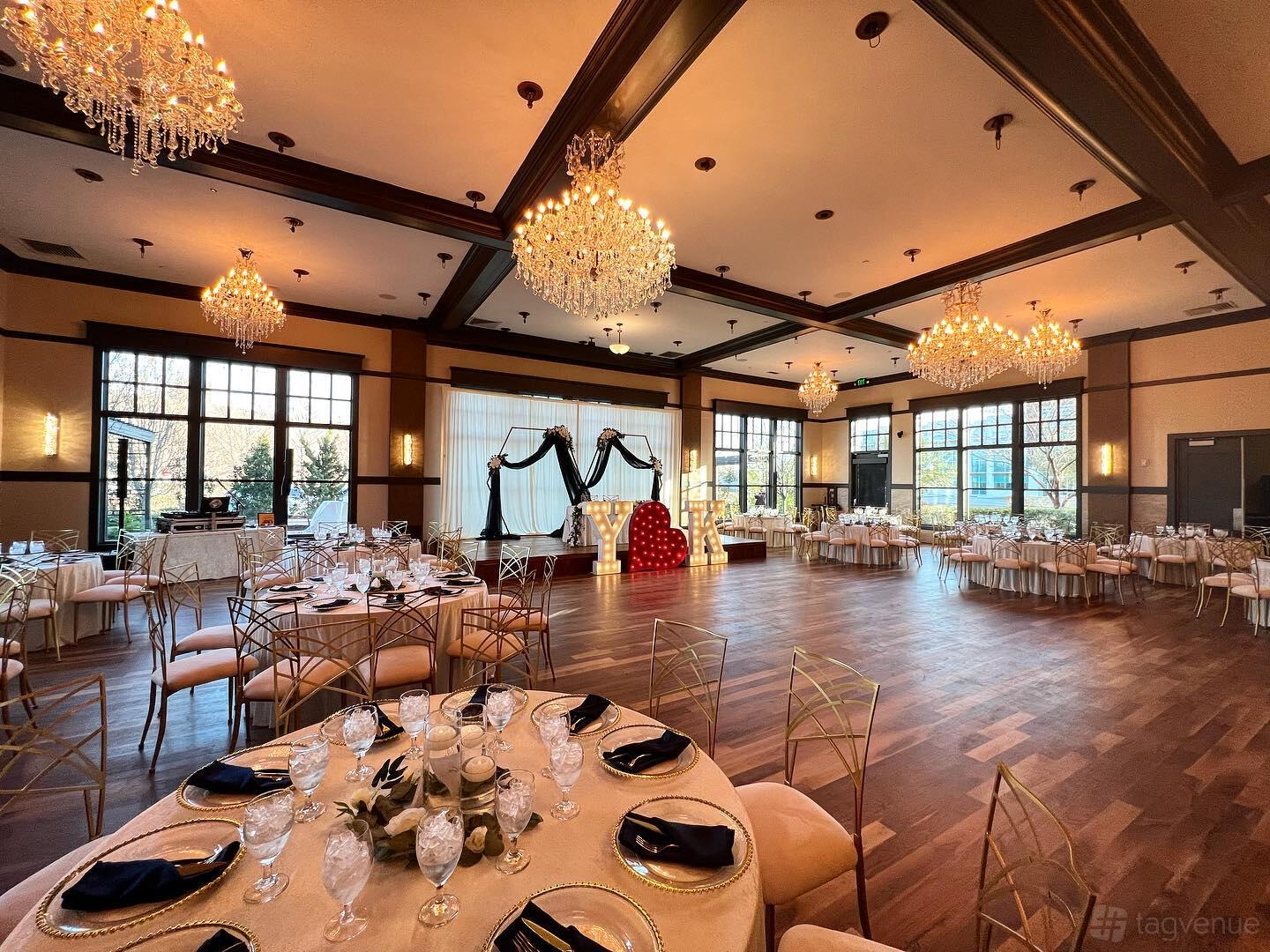 A dining room with crystal chandeliers, large windows, and round tables set for an event at Milano Event Center.