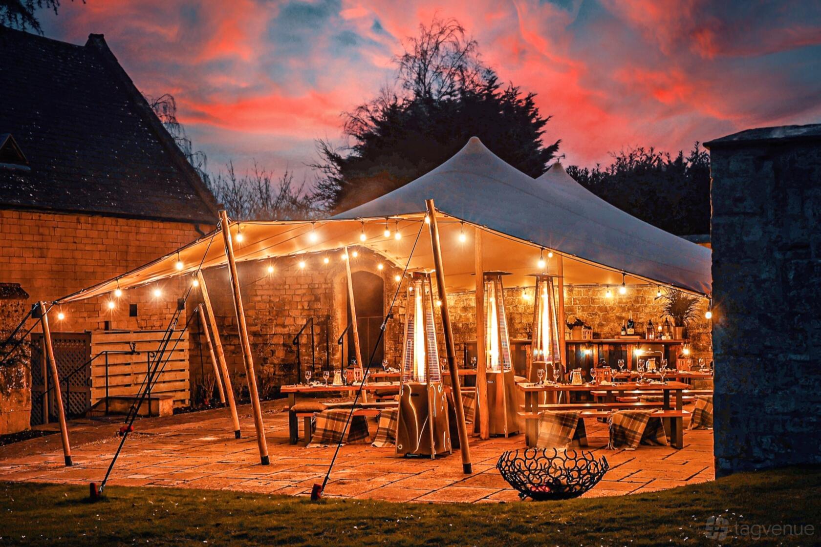 An outdoor event space with a stretch tent, string lights, and patio heaters at Ellenborough Park.