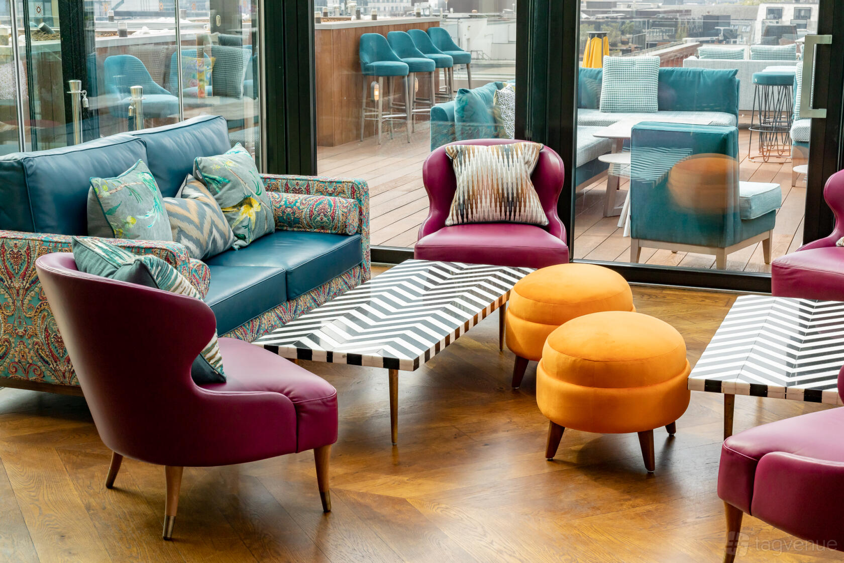 A rooftop bar lounge with patterned armchairs, vibrant ottomans, and a chevron coffee table at Aviary Rooftop Bar & Restaurant.
